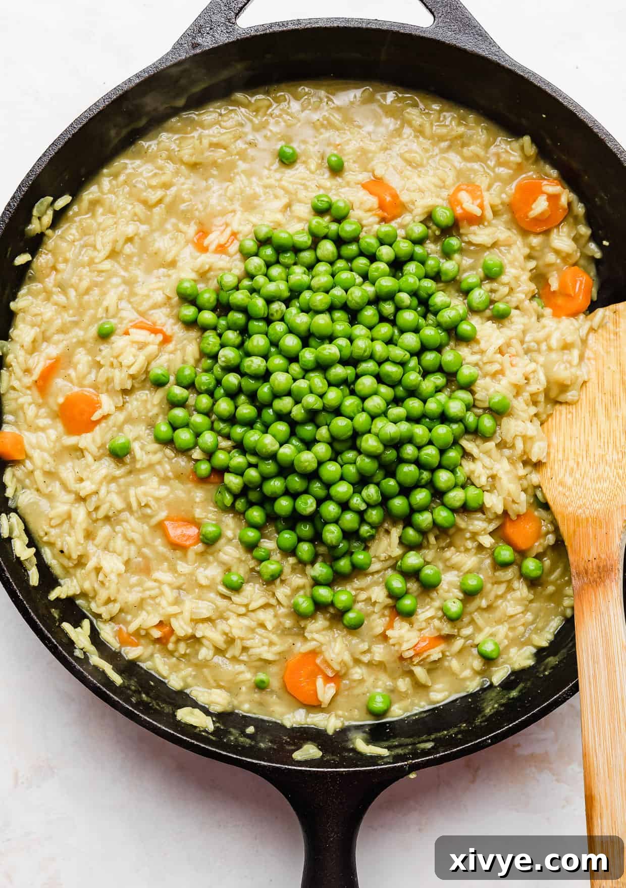 Caribbean Curried Chicken with Coconut Rice and Beans 8 Frozen peas being stirred into a skillet filled with Curry Chicken Rice and Peas recipe.