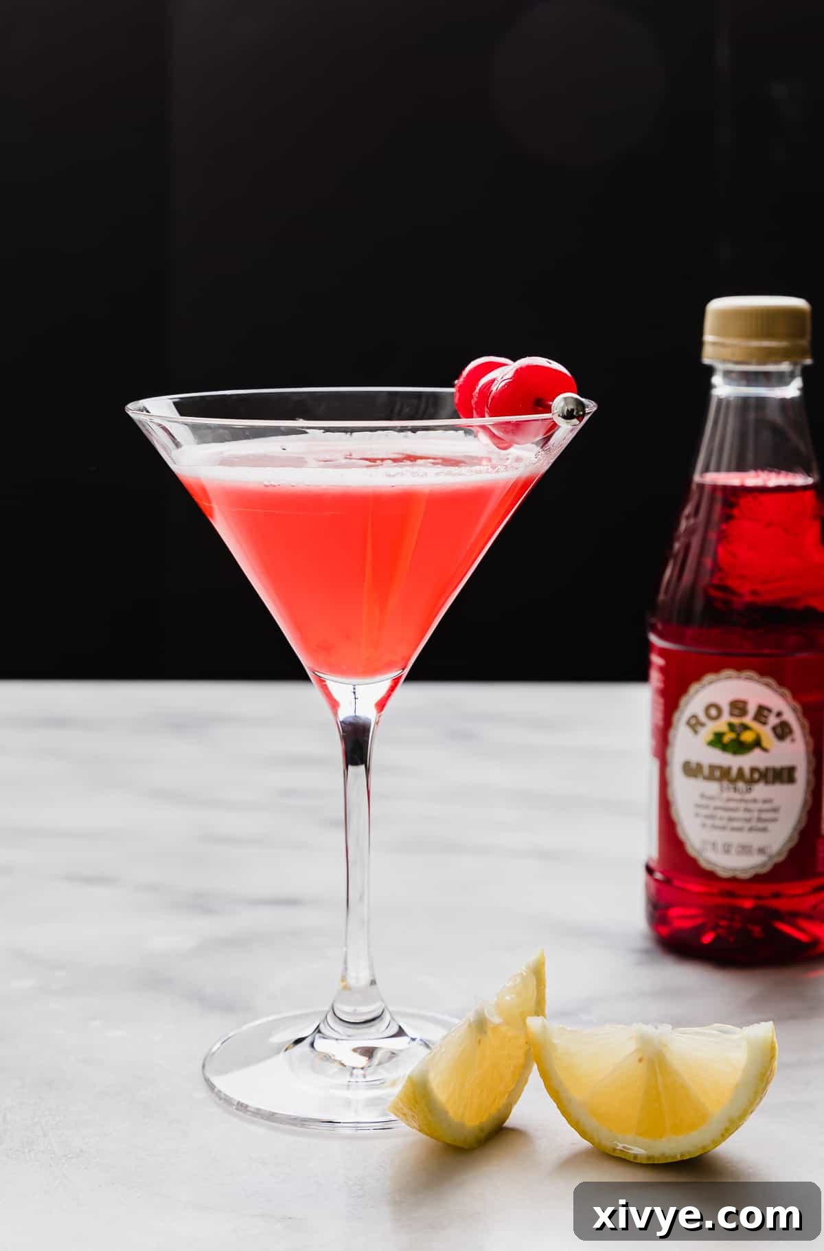 Pink Elegance Sparkler 2 A martini glass filled with a bright Pink Lady Mocktail and garnished with maraschino cherries, against a black background.