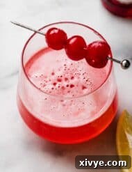 Pink Elegance Sparkler 7 Pink Lady Mocktail in a small glass with three maraschino cherries on a cocktail stick.