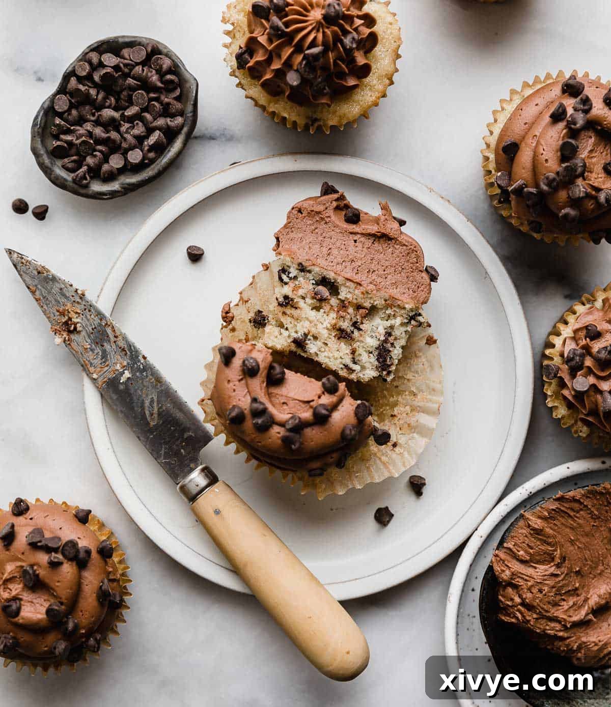 Fluffy Chocolate Chip Dream Cupcakes 6 A Chocolate Chip Cupcake on a white plate, cut in half with a knife to the left of the plate.