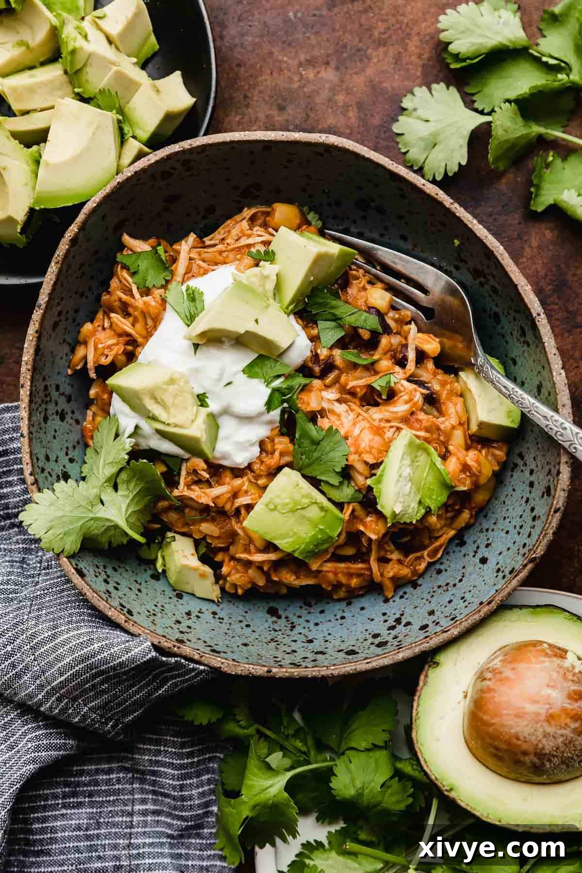 Instant Pot Chicken Taco Bowls in a blue bowl topped with sour cream, cilantro, and avocado. A visually appealing and healthy meal option.