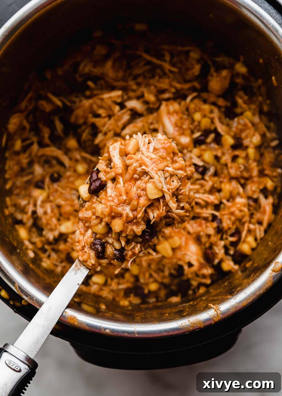 A large spoon holding Instant Pot Chicken Taco mixture on it, showing the rich texture and vibrant ingredients.