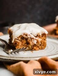 A square of Carrot Coffee Cake topped with pecan streusel and cream cheese glaze against a dark brown background.