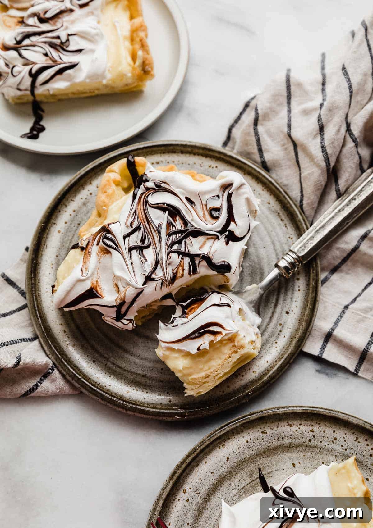 A square slice of homemade cream puff cake made with a cream puff crust and vanilla pudding and whipped cream topping, on a gray plate.