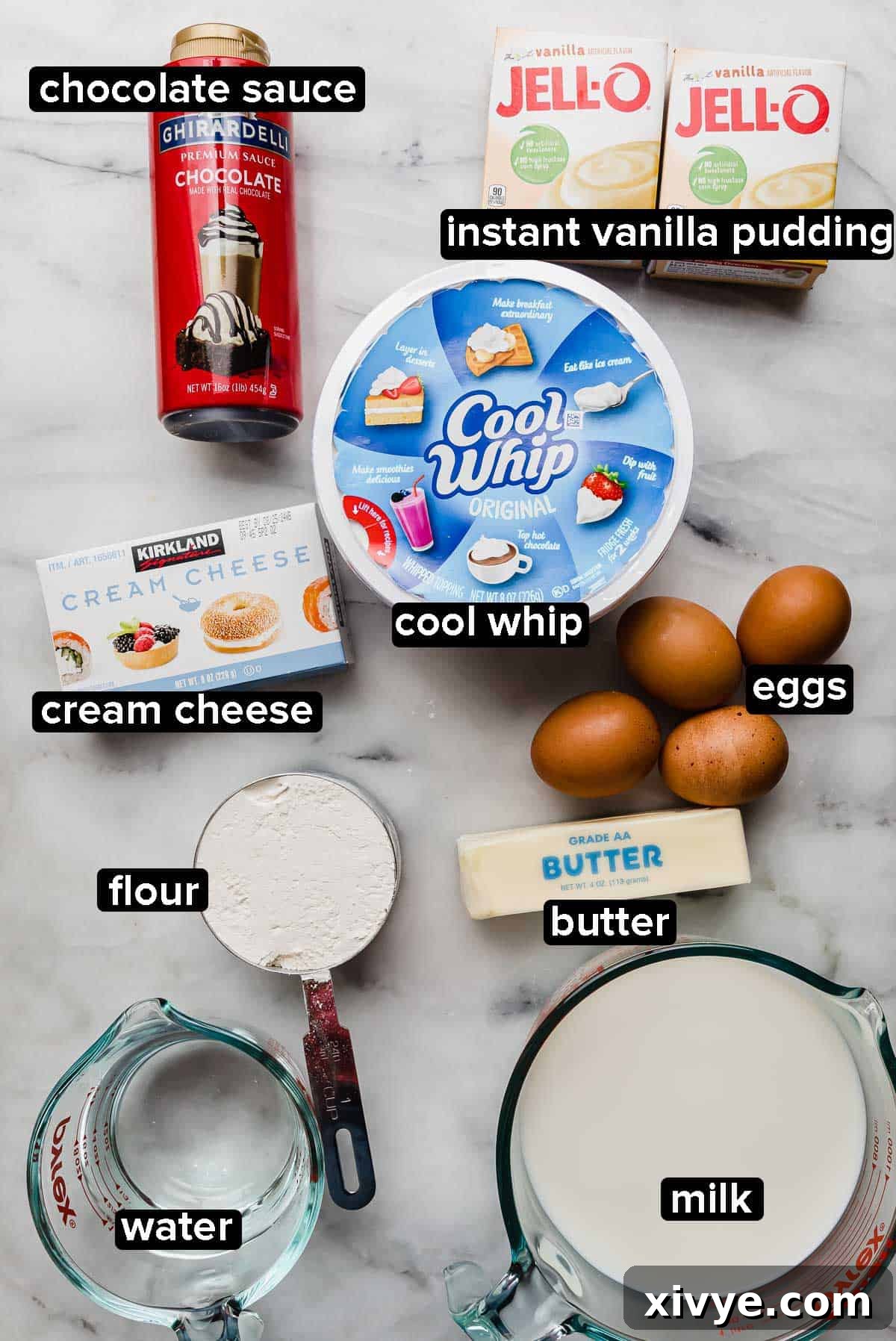 Cream Puff Cake recipe ingredients on a white marble table: instant vanilla pudding packets, cool whip, cream cheese, eggs, milk, water, butter, flour, and chocolate syrup.