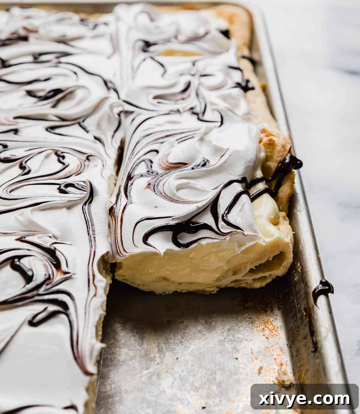 A photo of cream puff cake in a baking sheet, topped with cool whip and chocolate syrup.