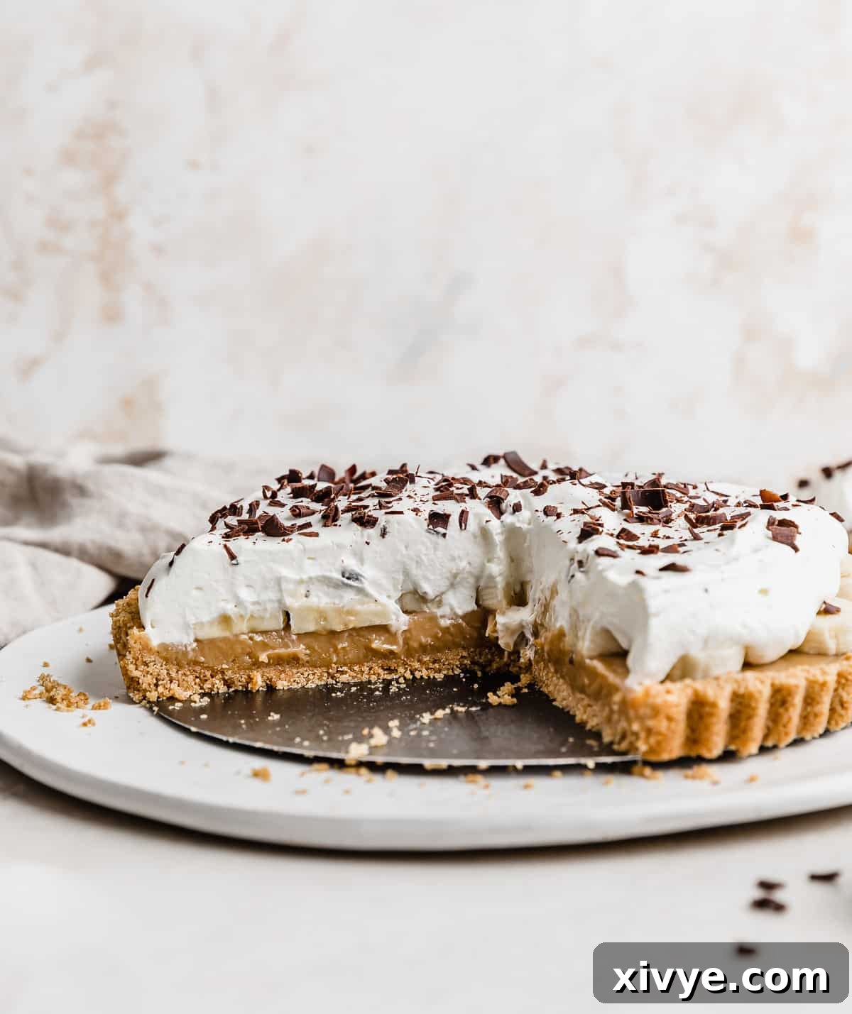 Decadent Banoffee Pie with Crunchy Graham Crust 2 A Banoffee Pie on a white plate, topped with whipped cream and chocolate shavings.