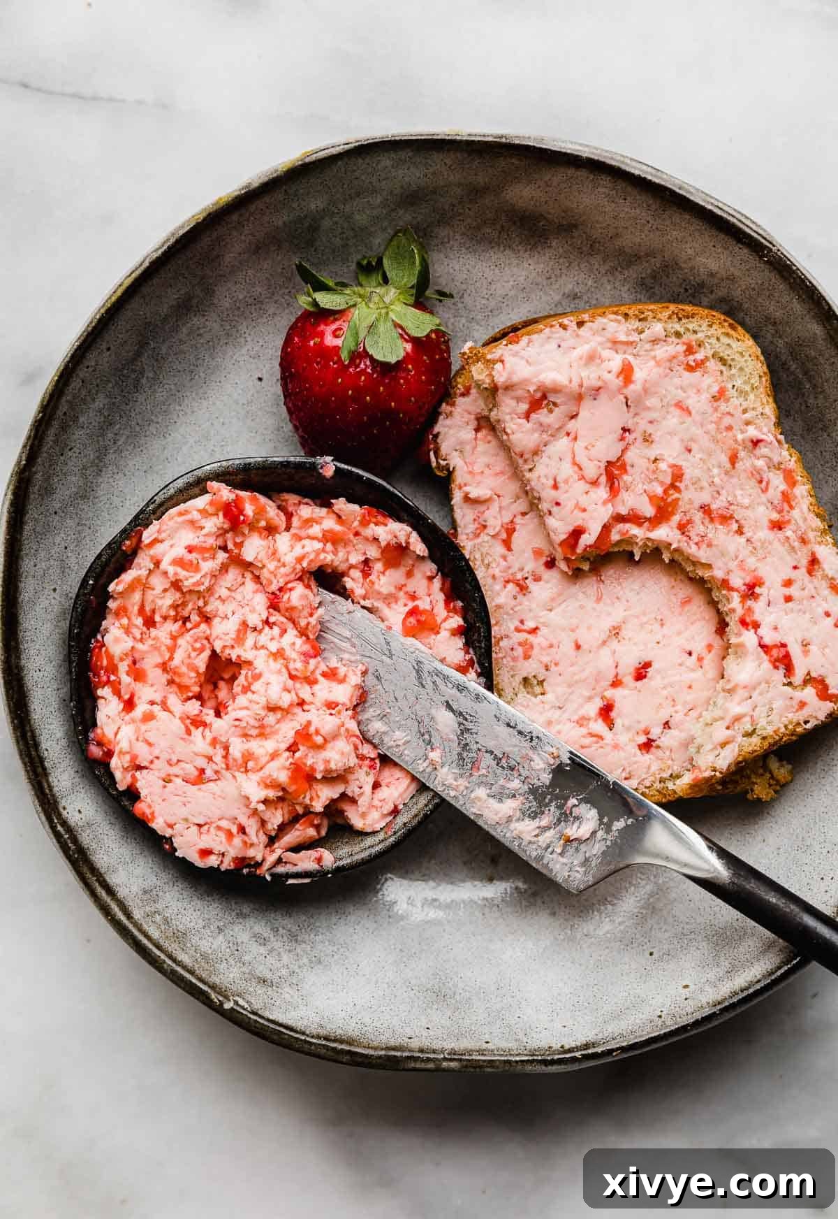 Fresh Strawberry Butter in a small black bowl, with chunky strawberry butter spread over two slices of toasted bread.