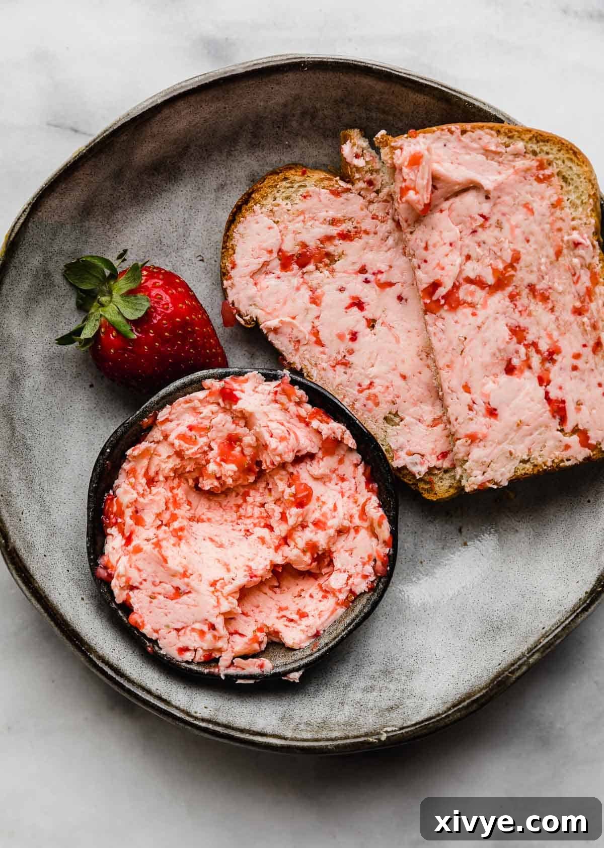 Strawberry Butter smeared on two slices of bread on a gray plate.