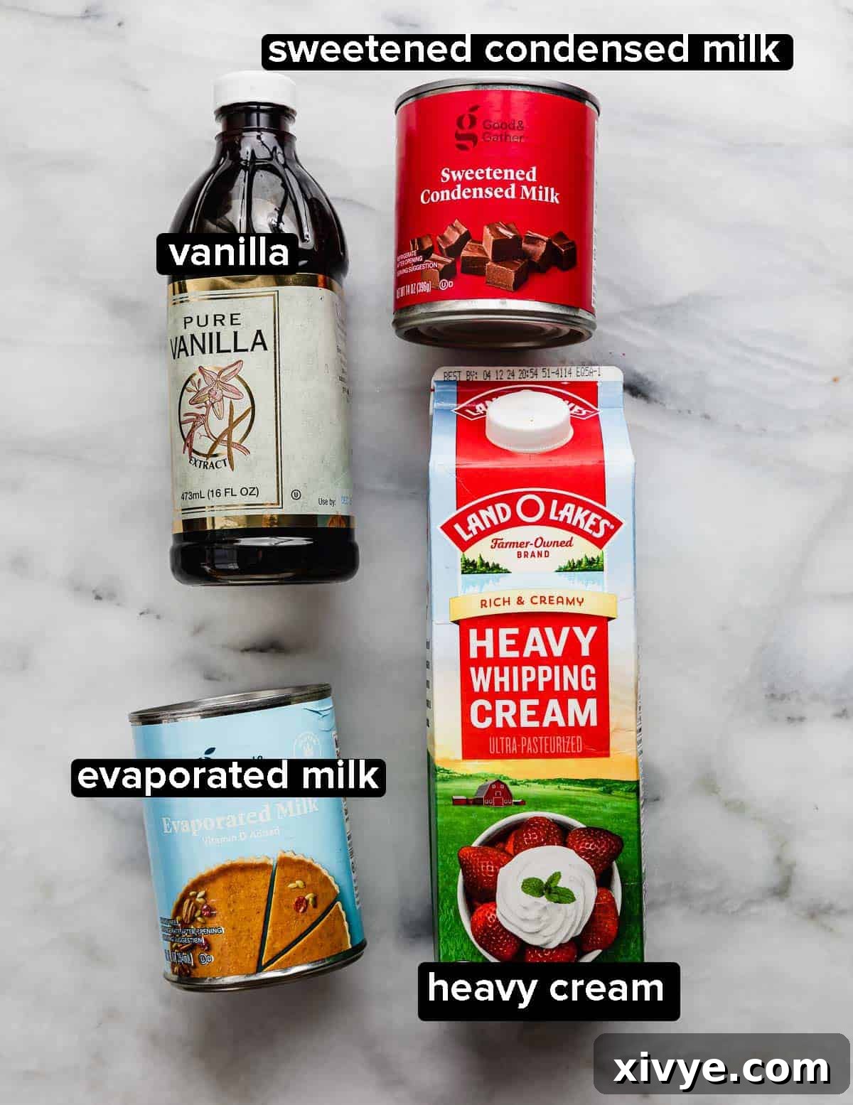 Heavenly Mexican Tres Leches Cake 4 Three milks (evaporated milk, sweetened condensed milk, and heavy cream) paired with a bottle of vanilla extract on a marble surface.