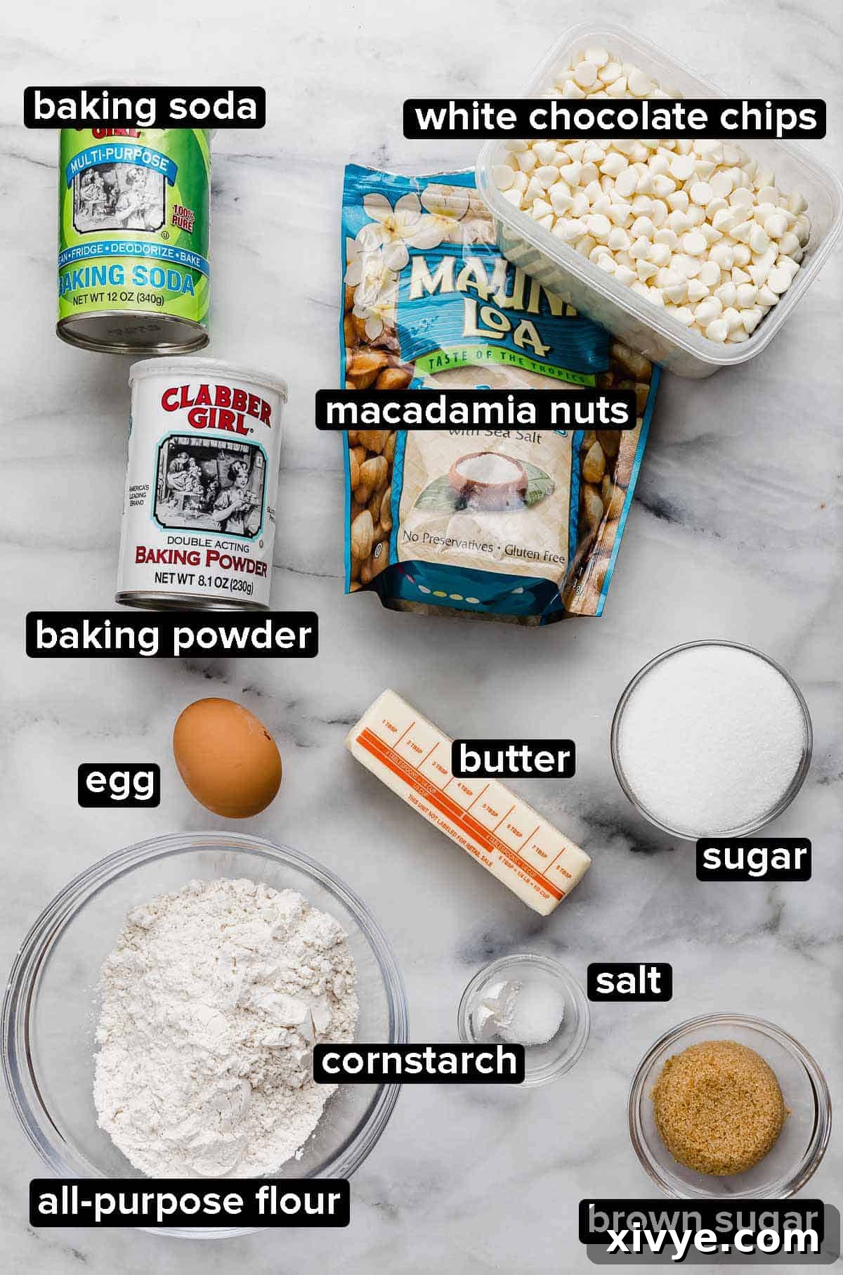 Gourmet White Chocolate Macadamia Treats 3 White Chocolate Macadamia Nut Cookies ingredients on a white marble surface: flour, butter, baking powder and soda, cornstarch, salt, sugar, egg, white chocolate chips and salted macadamia nuts.