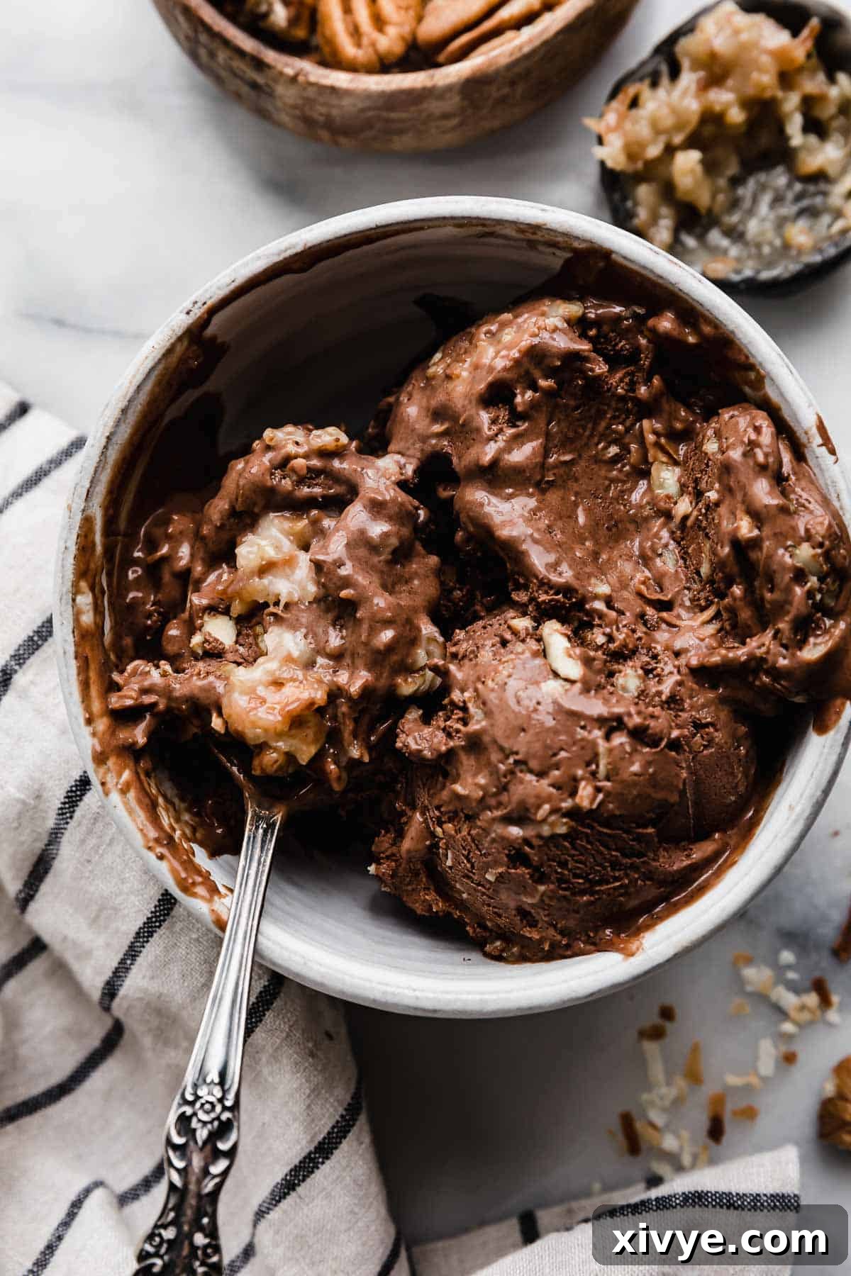 The best German Chocolate Cake Ice Cream in a white bowl, with a spoon scooping out some of the coconut pecan chocolate ice cream.
