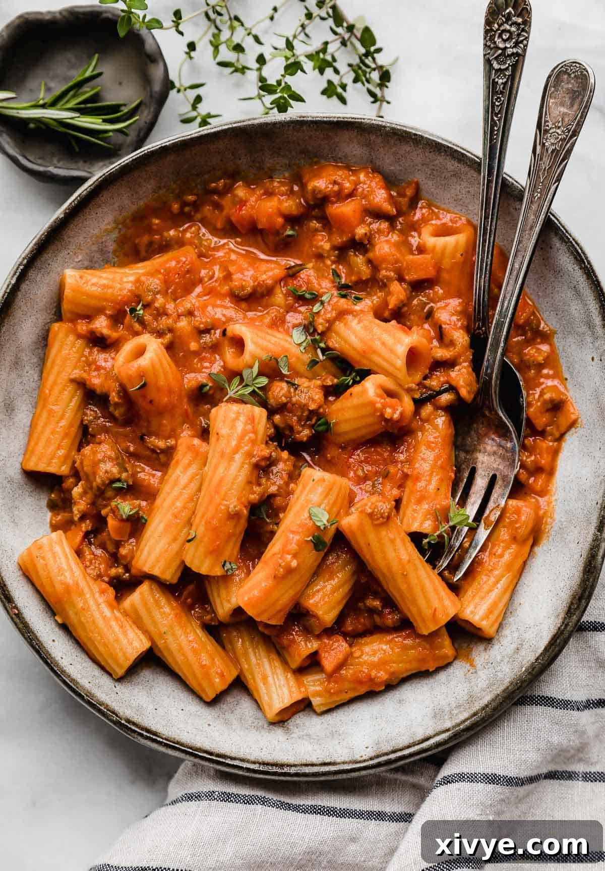 Rustic Sausage Ragu 2 A gray pasta bowl filled with creamy Sausage Ragu with fresh herbs on a white surface, ready to be enjoyed.