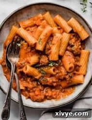 Rustic Sausage Ragu 9 A fork and spoon in the bowl accompanied with delicious Sausage Ragu, on a white marble surface, ready to be served.