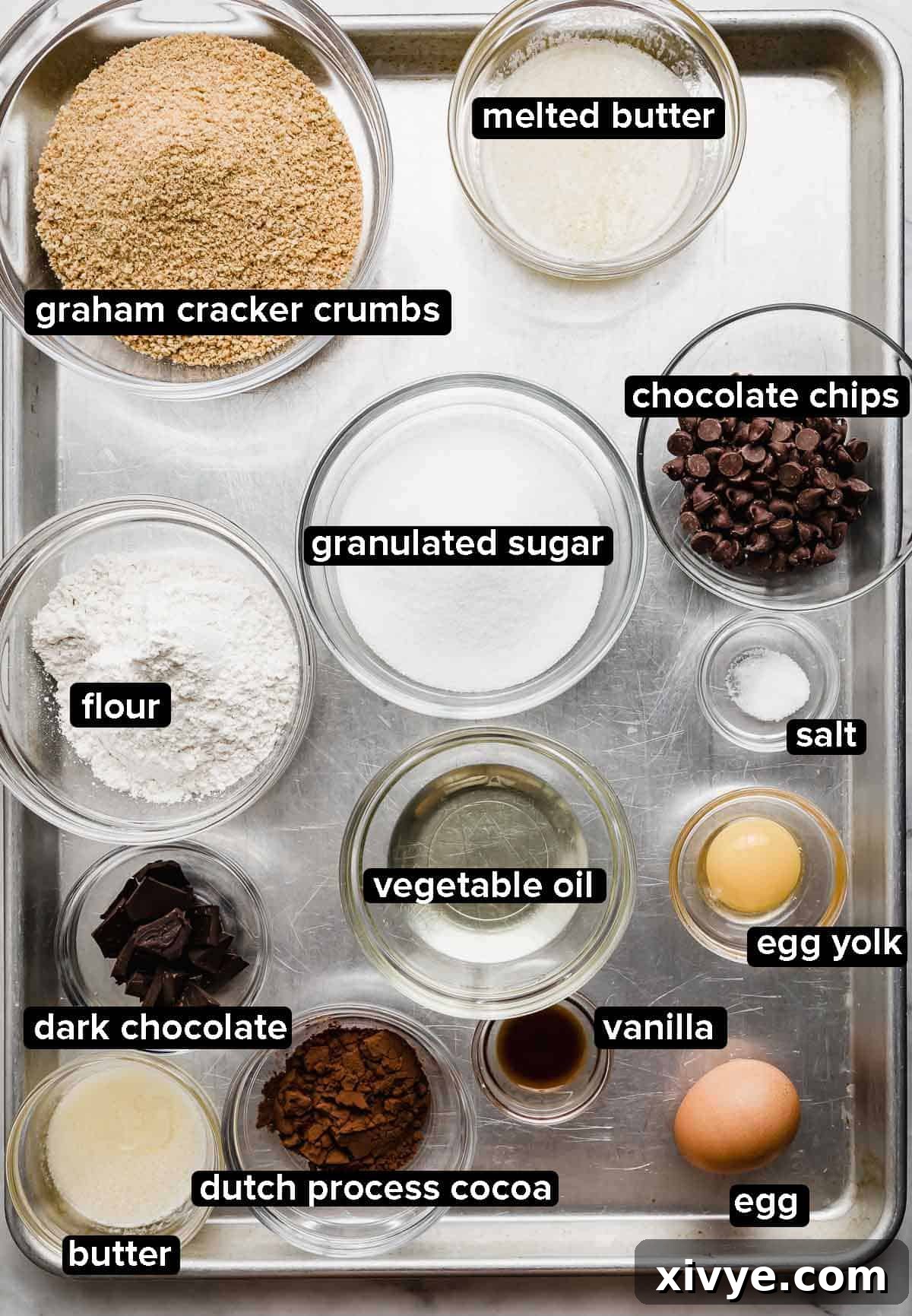 Gooey Campfire Brownies 3 S'mores Brownies ingredients portioned into glass bowls on a silver baking sheet. A beautiful array of baking essentials.