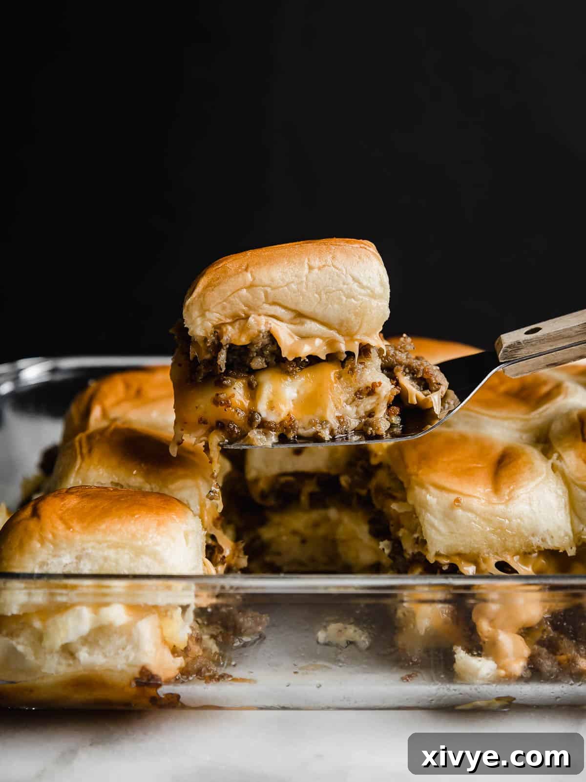 A Hawaiian Roll Breakfast Sliders recipe being held up on a metal spatula against a black background.