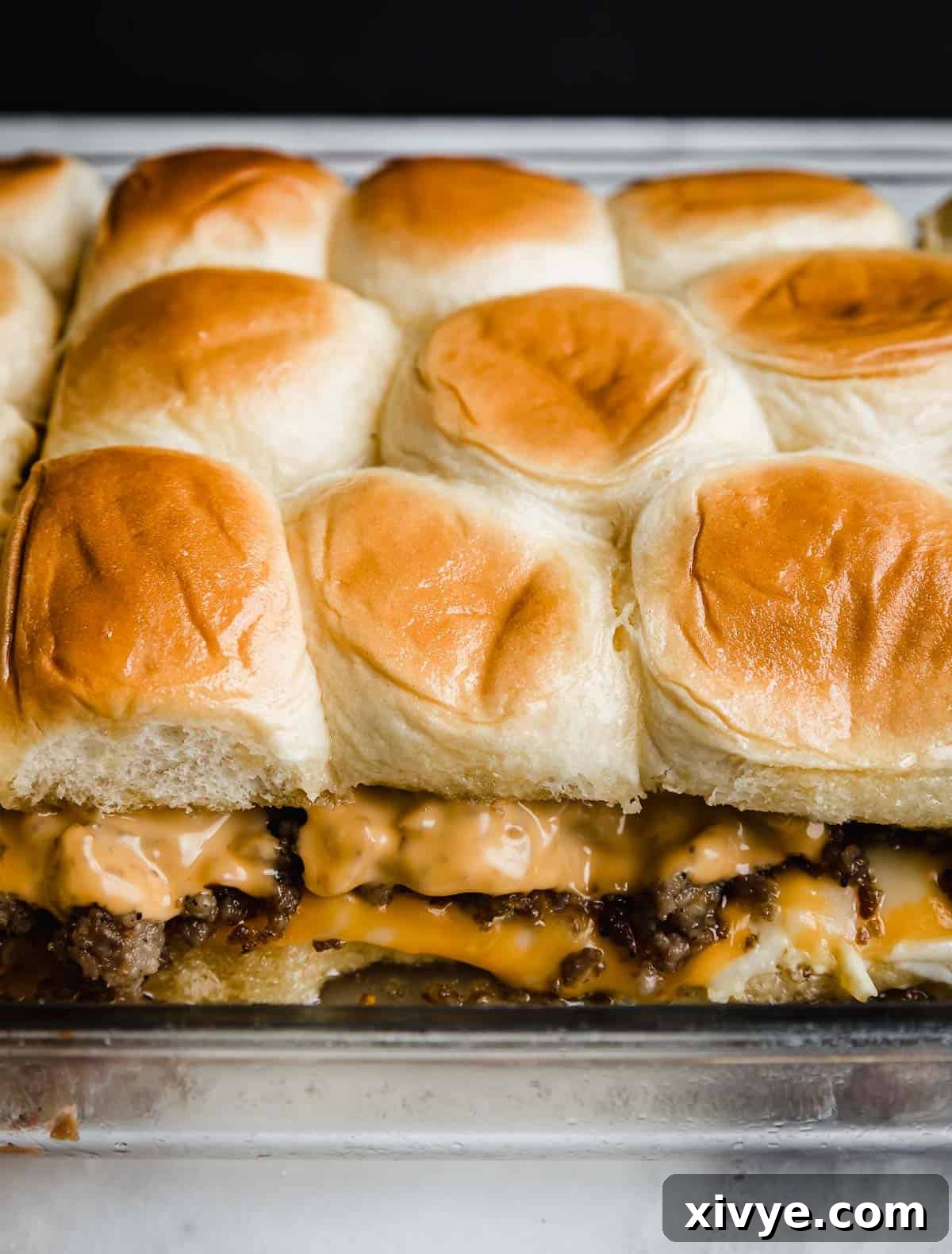 Baked Hawaiian Roll Breakfast Sliders in a glass baking pan showing the layers of scrambled eggs, cheese, and sausage.