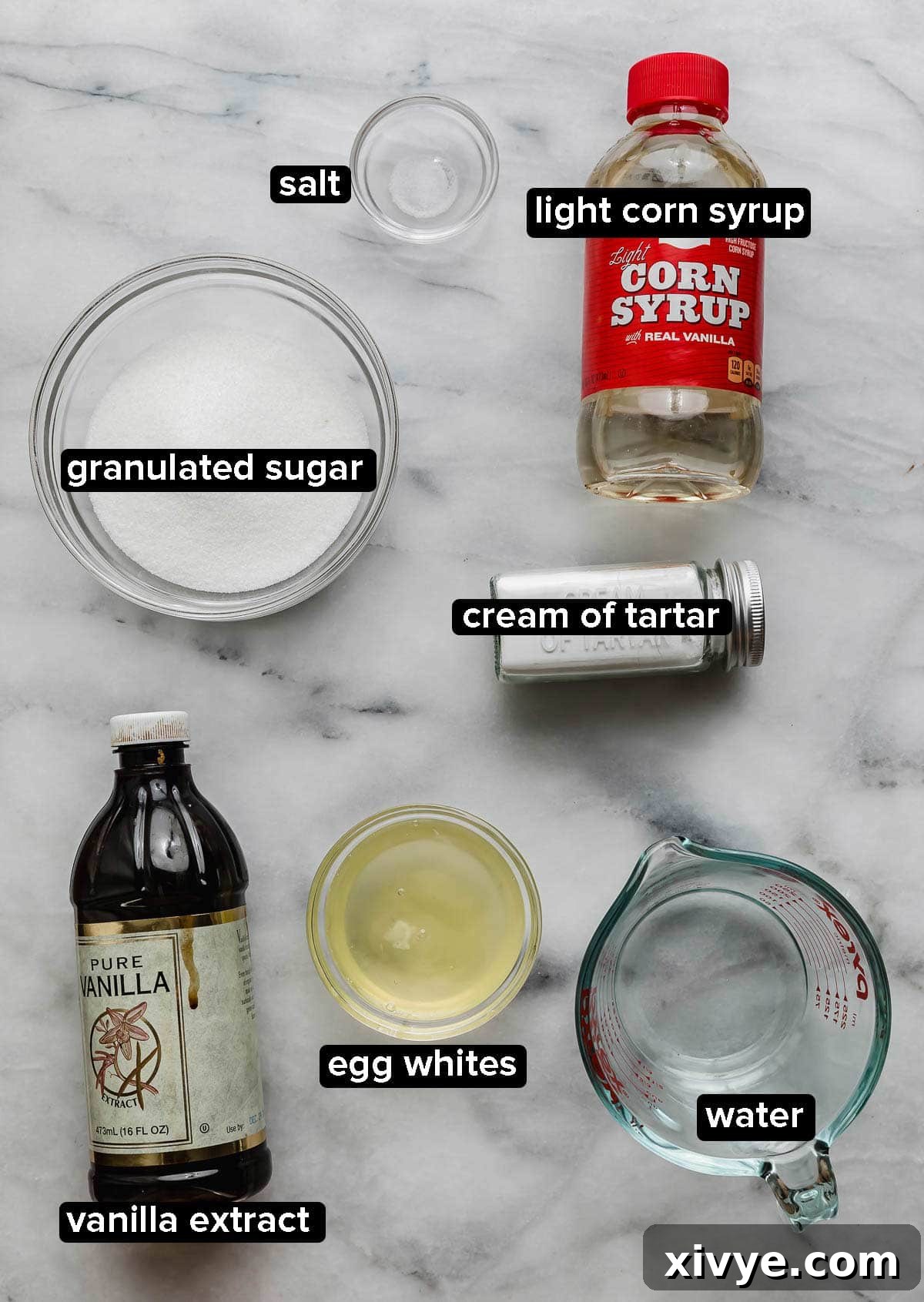 Homemade Marshmallow Cream ingredients on a white marble surface: egg whites, corn syrup, vanilla, water, sugar, and cream of tartar.