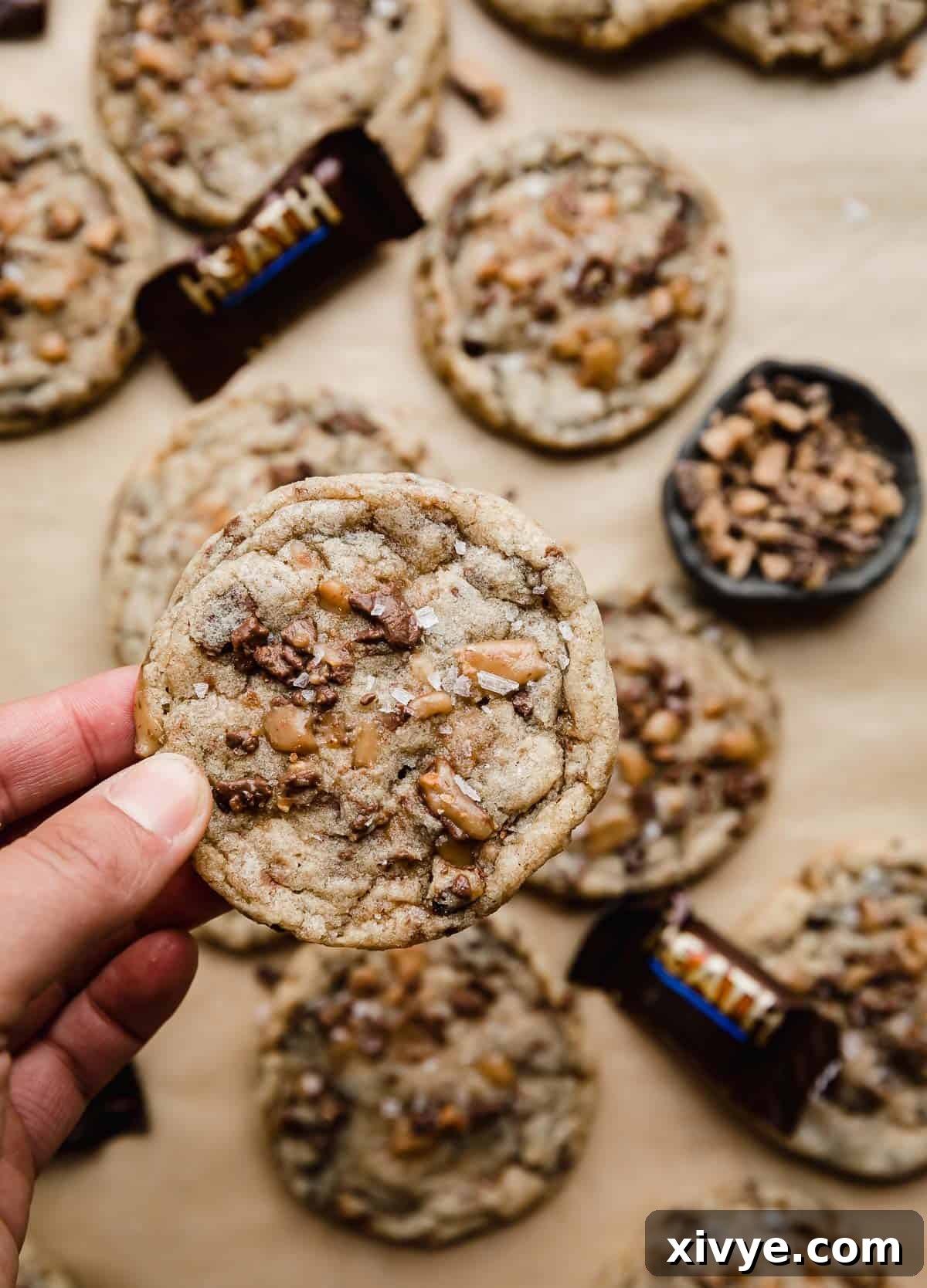 Toffee Crunch Cookies 2 Heath Bar Cookies recipe with lots of Heath bits in the cookie and on top, and a hand holding up one of the best Heath cookies.