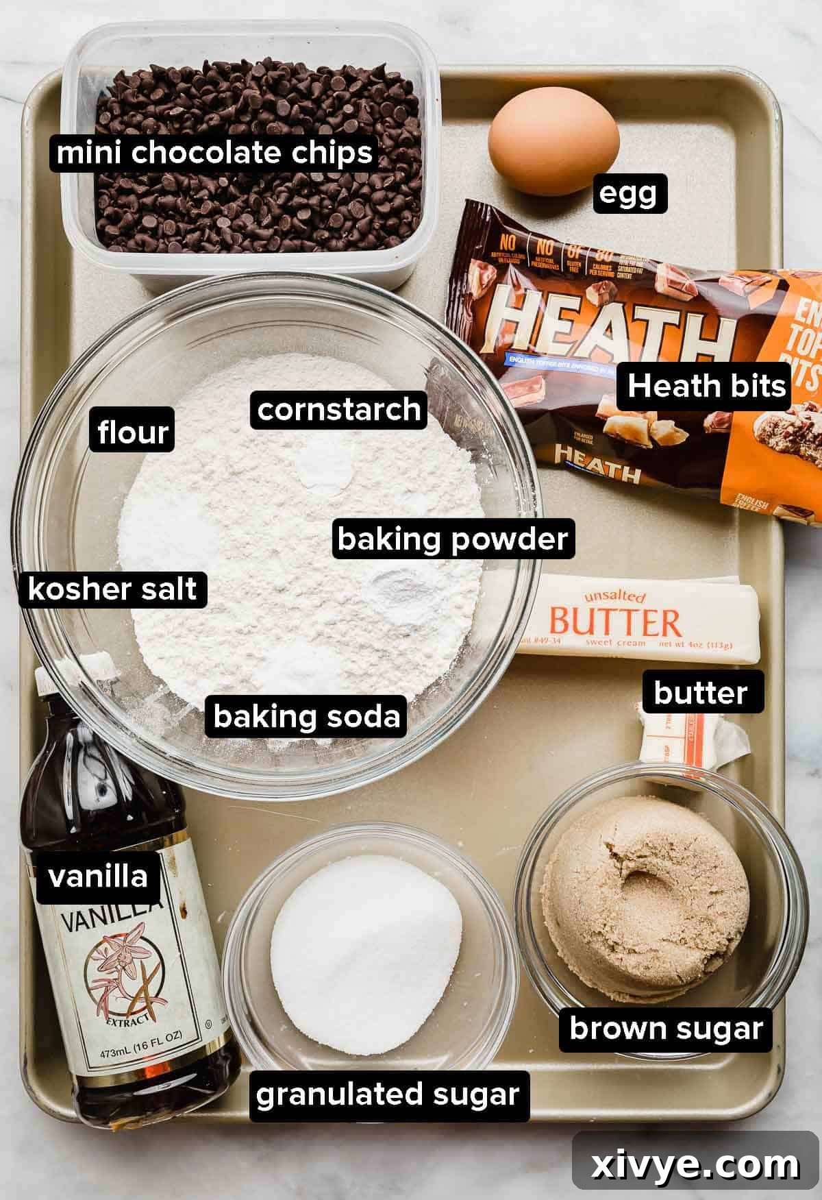 Toffee Crunch Cookies 3 Heath Bar Cookies ingredients portioned into glass bowls on a gold baking sheet, including Heath bits and mini chocolate chips.