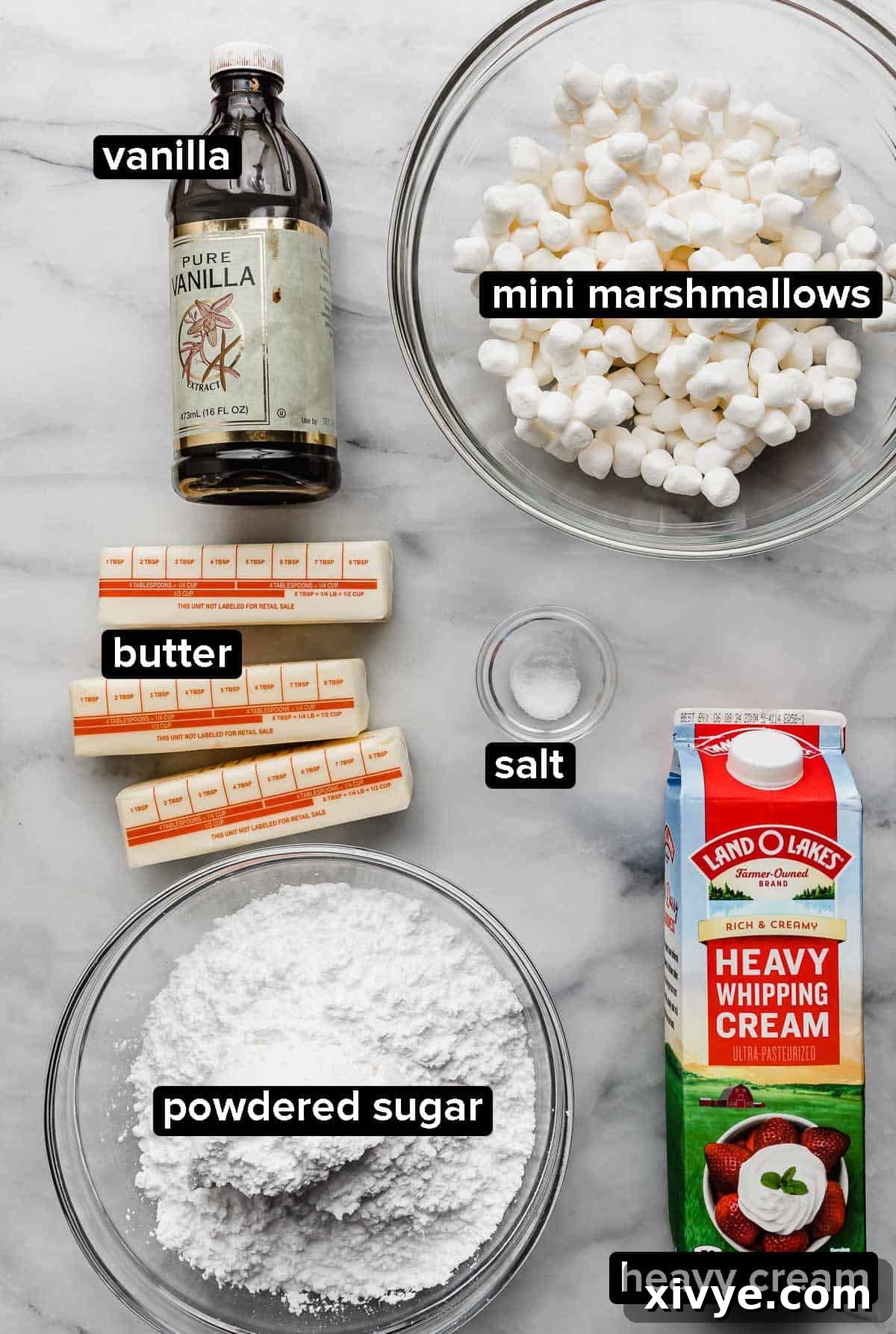 Toasted Marshmallow Frosting ingredients on a white surface: heavy cream, mini marshmallows, powdered sugar, butter, and vanilla extract are neatly arranged.