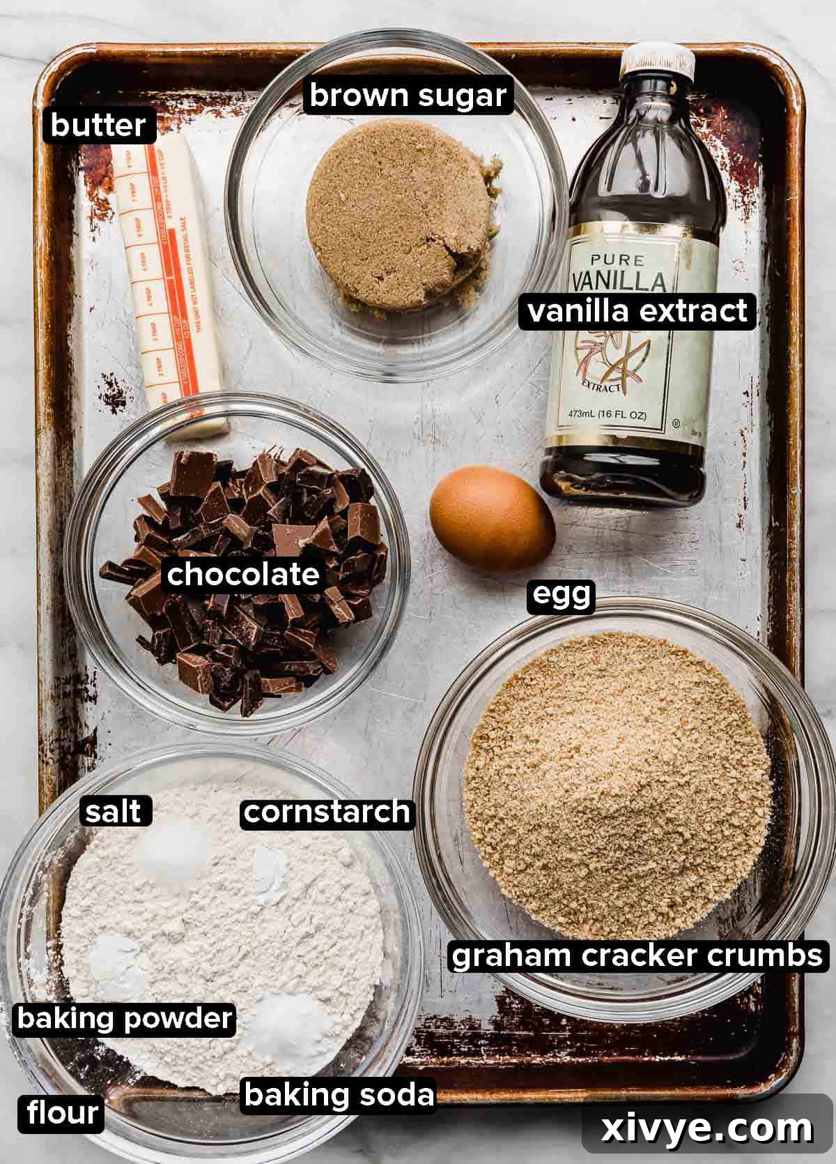 S'mores Cookie ingredients on a baking sheet: sugar, chocolate, graham cracker crumbs, butter, egg, and dry ingredients.