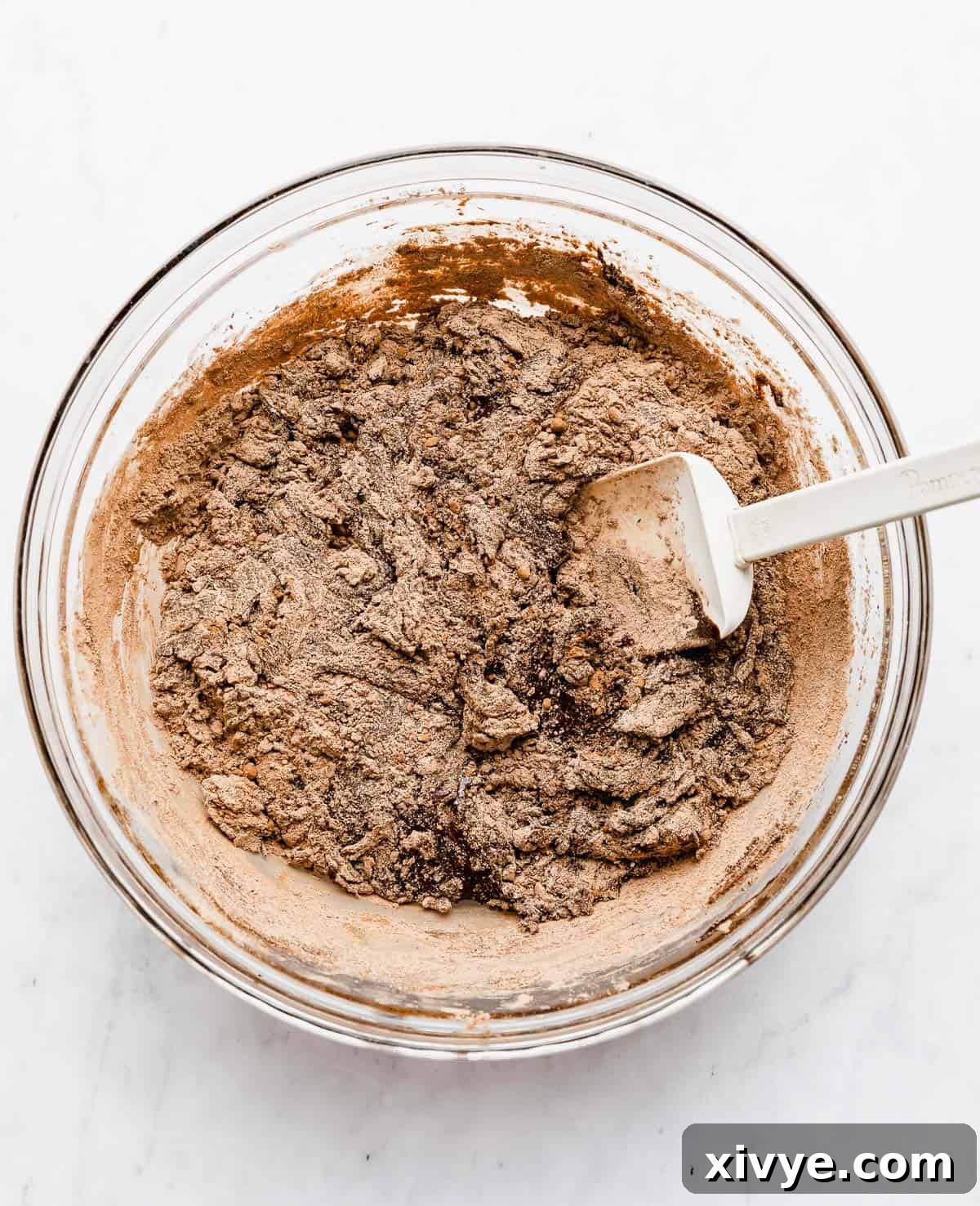 A light brown flour mixture being carefully folded into the rich chocolate wet ingredients using a spatula, forming the cookie dough.