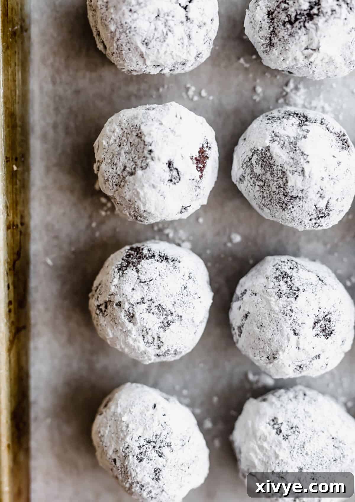 Chocolate Crinkle Cookie dough balls, perfectly coated in both granulated and powdered sugar, lined up neatly on a baking sheet, ready for the oven.