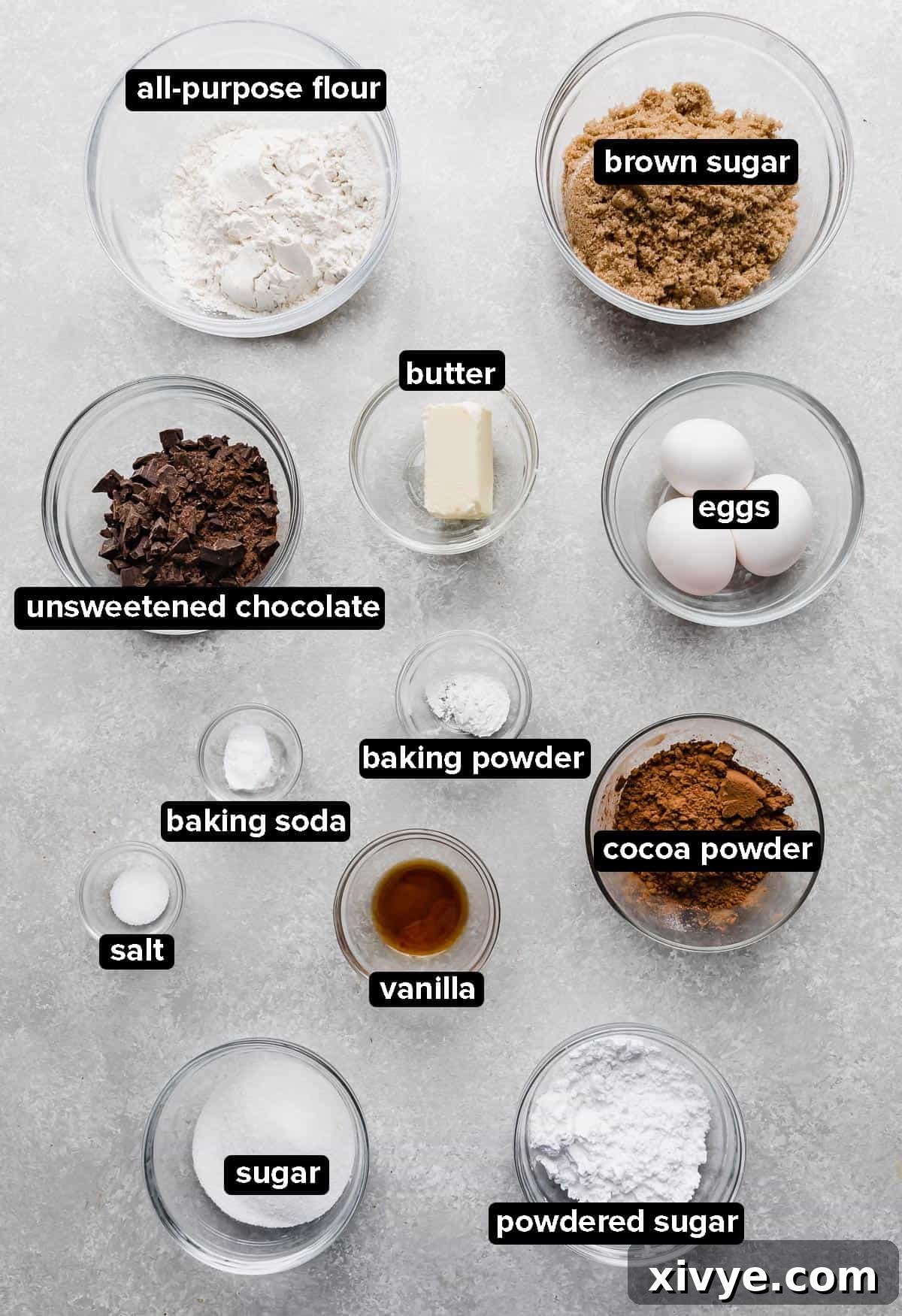 Chocolate Crinkle Cookie ingredients laid out in glass bowls on a gray background, ready for baking.