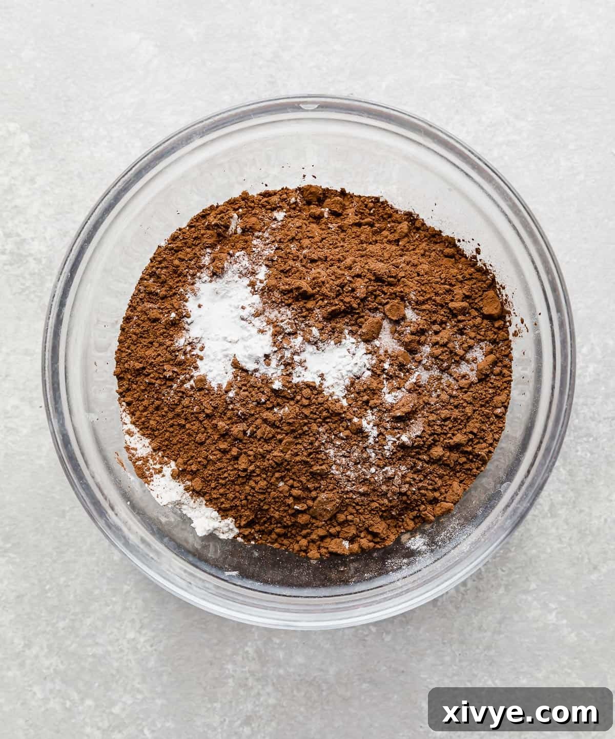 Flour, cocoa powder, baking powder, baking soda, and salt in a glass bowl, prepared for making chocolate crinkle cookies.