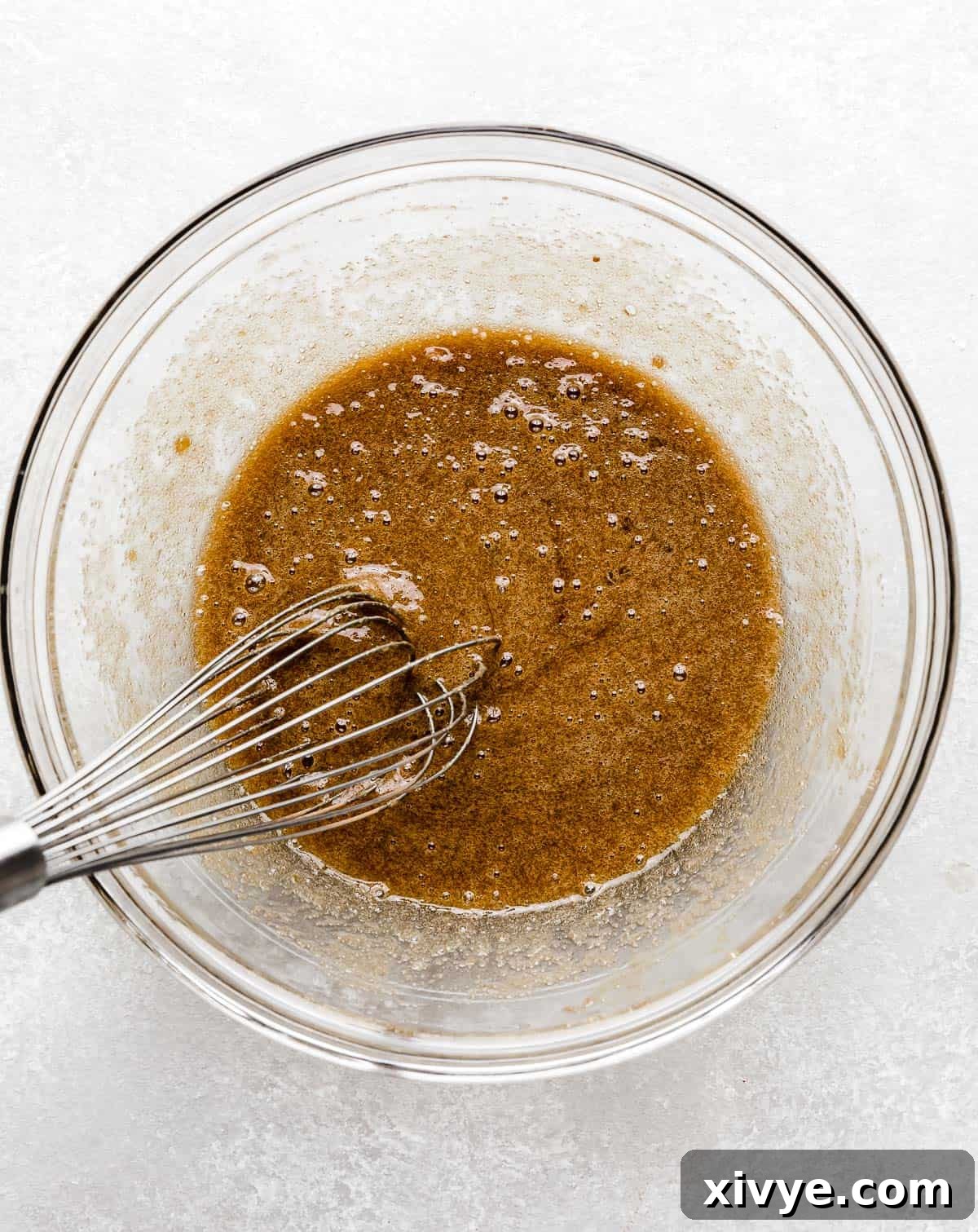 A whisk blending the brown sugar, eggs, and vanilla mixture into a smooth, cohesive liquid in a glass bowl.