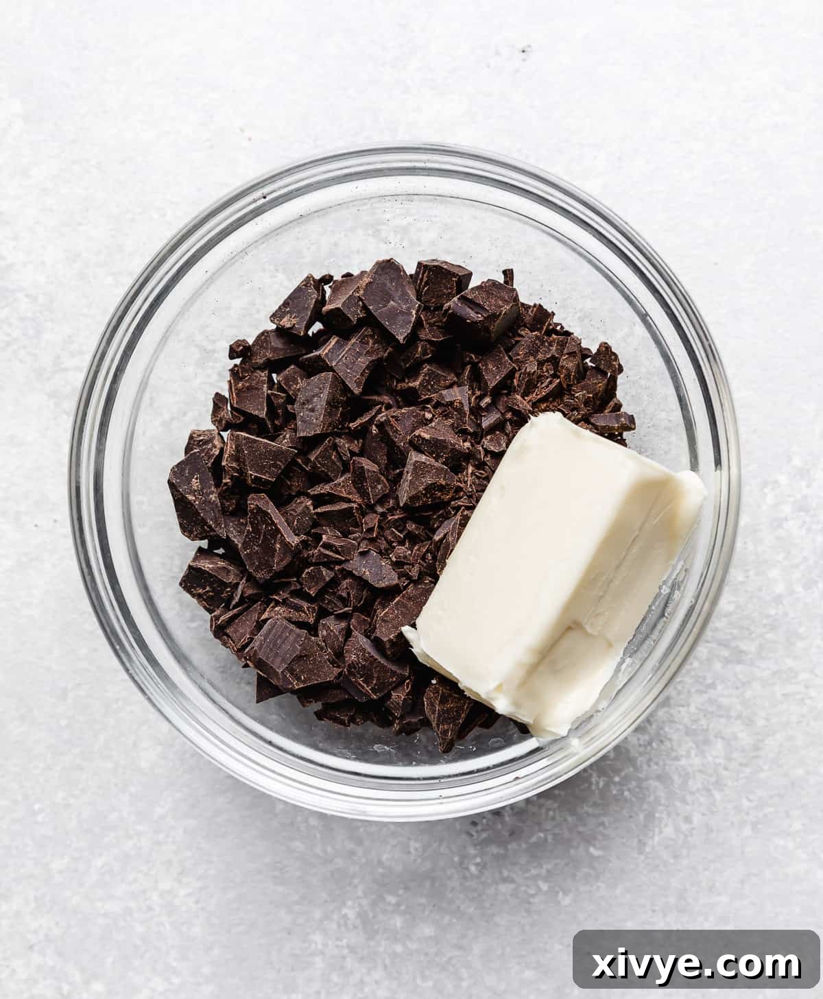 A stick of unsalted butter and finely chopped unsweetened chocolate in a glass bowl, awaiting melting.