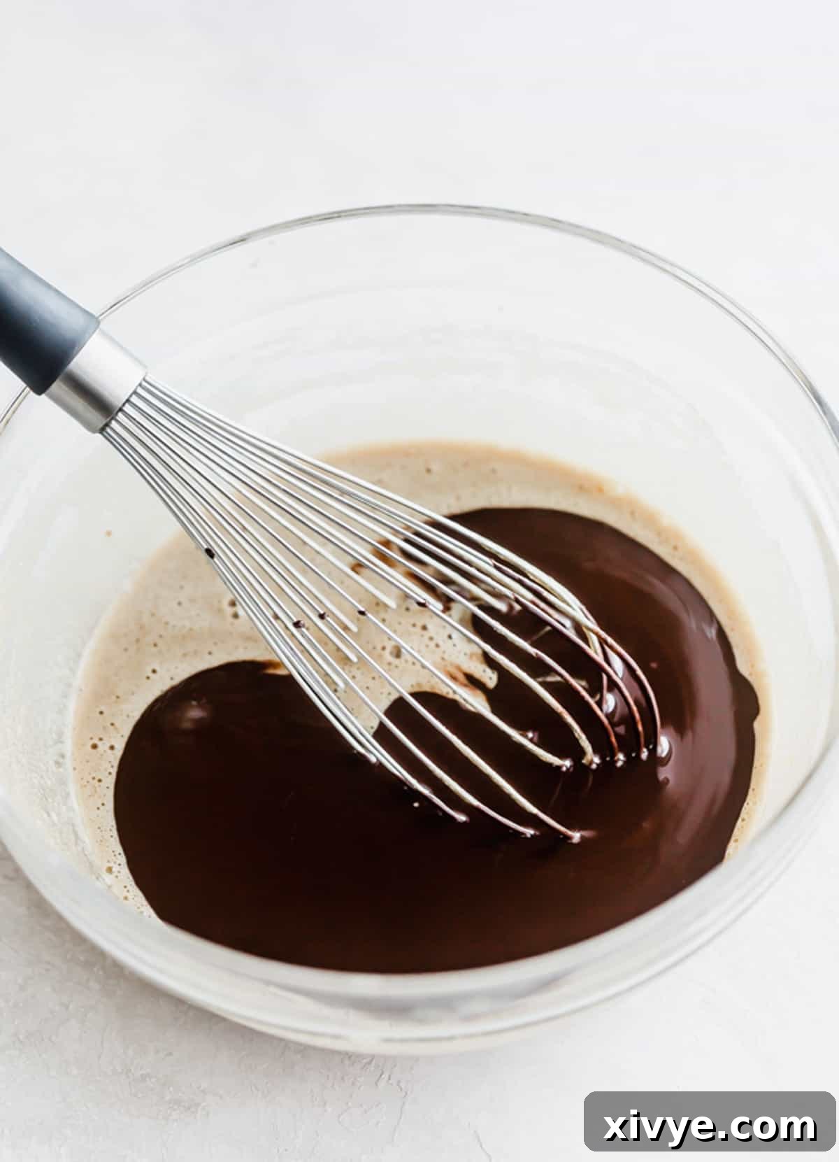 A whisk expertly stirring melted butter and chocolate together until a smooth, glossy mixture is formed.