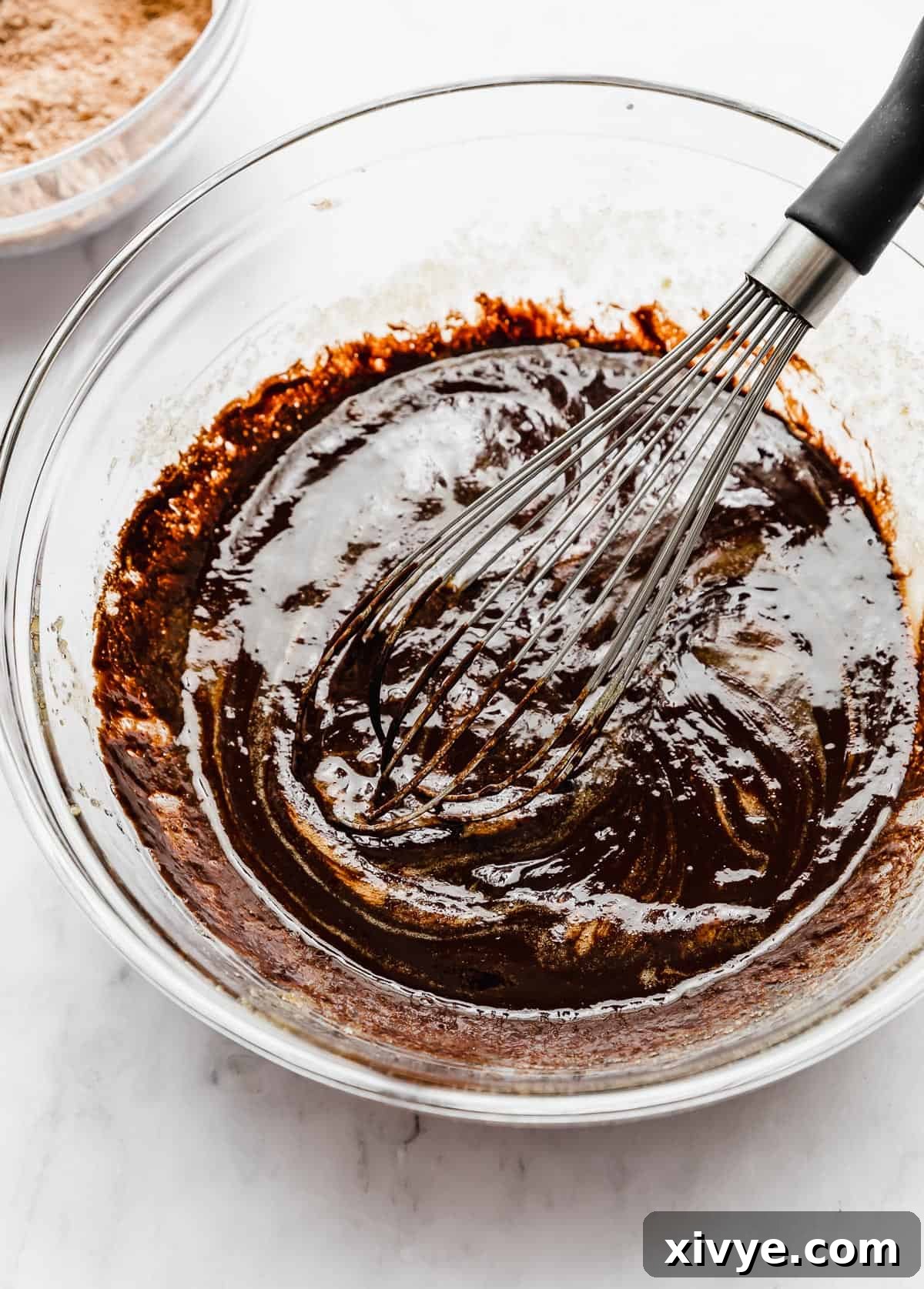 A smooth, dark chocolate mixture being gently stirred into the wet ingredients with a whisk, creating a rich dough base.