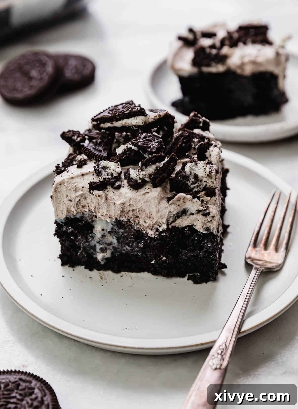 A square slice of Oreo Poke Cake drizzled with sweetened condensed milk and topped with a whipped Oreo cream pudding frosting, showcasing its layers and rich texture.