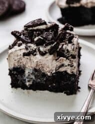 A slice of an Oreo Poke Cake recipe on a white plate, the easy Oreo sheet cake features a black cake base, sweetened condensed milk, and an easy Oreo pudding frosting.