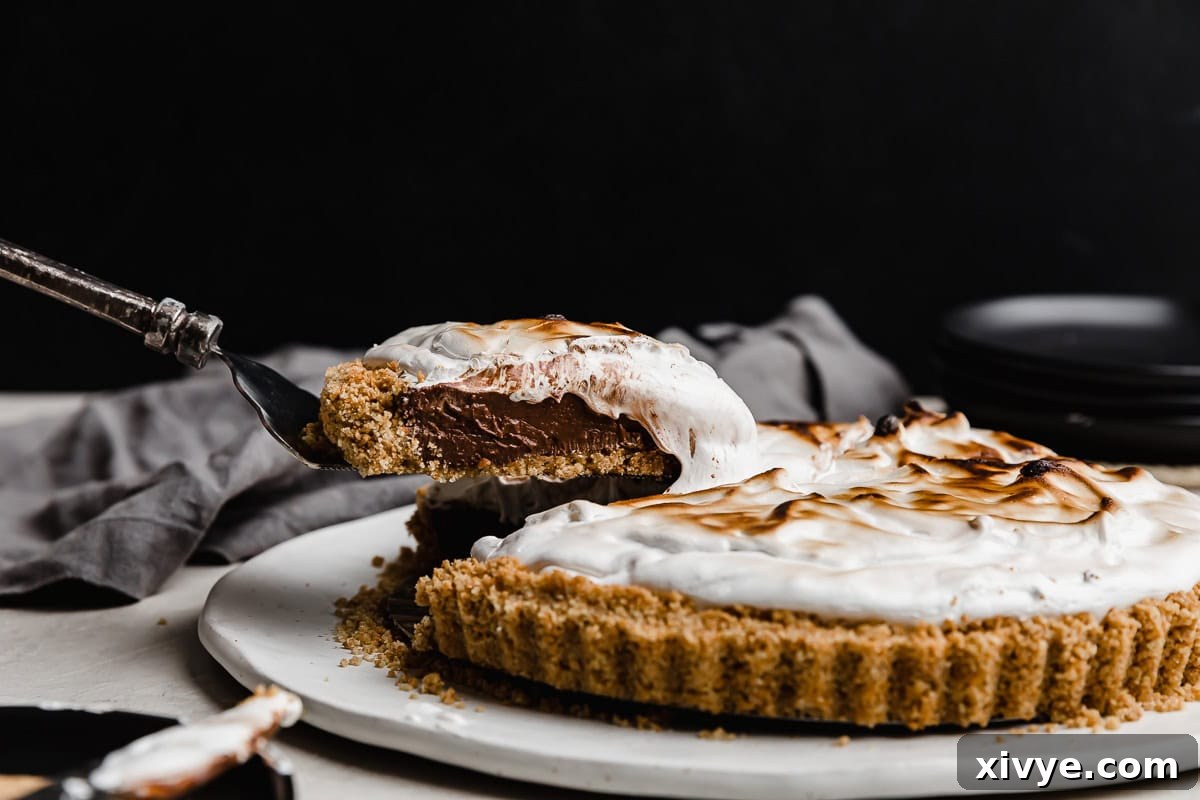 A slice of homemade S'mores Pie balanced on a pie spatula hovering against a black background.