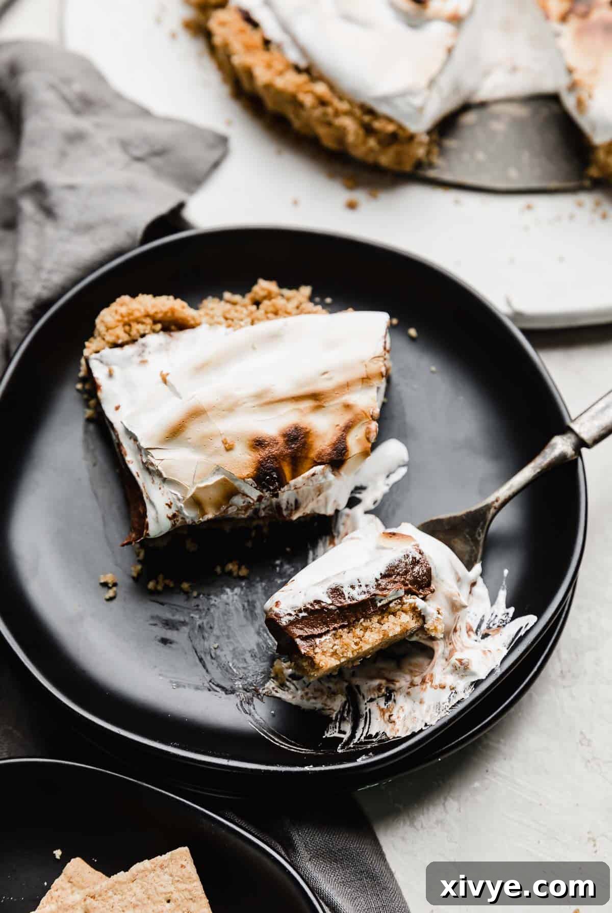A slice of S'mores Pie on a black plate with a fork cutting into a chunk.