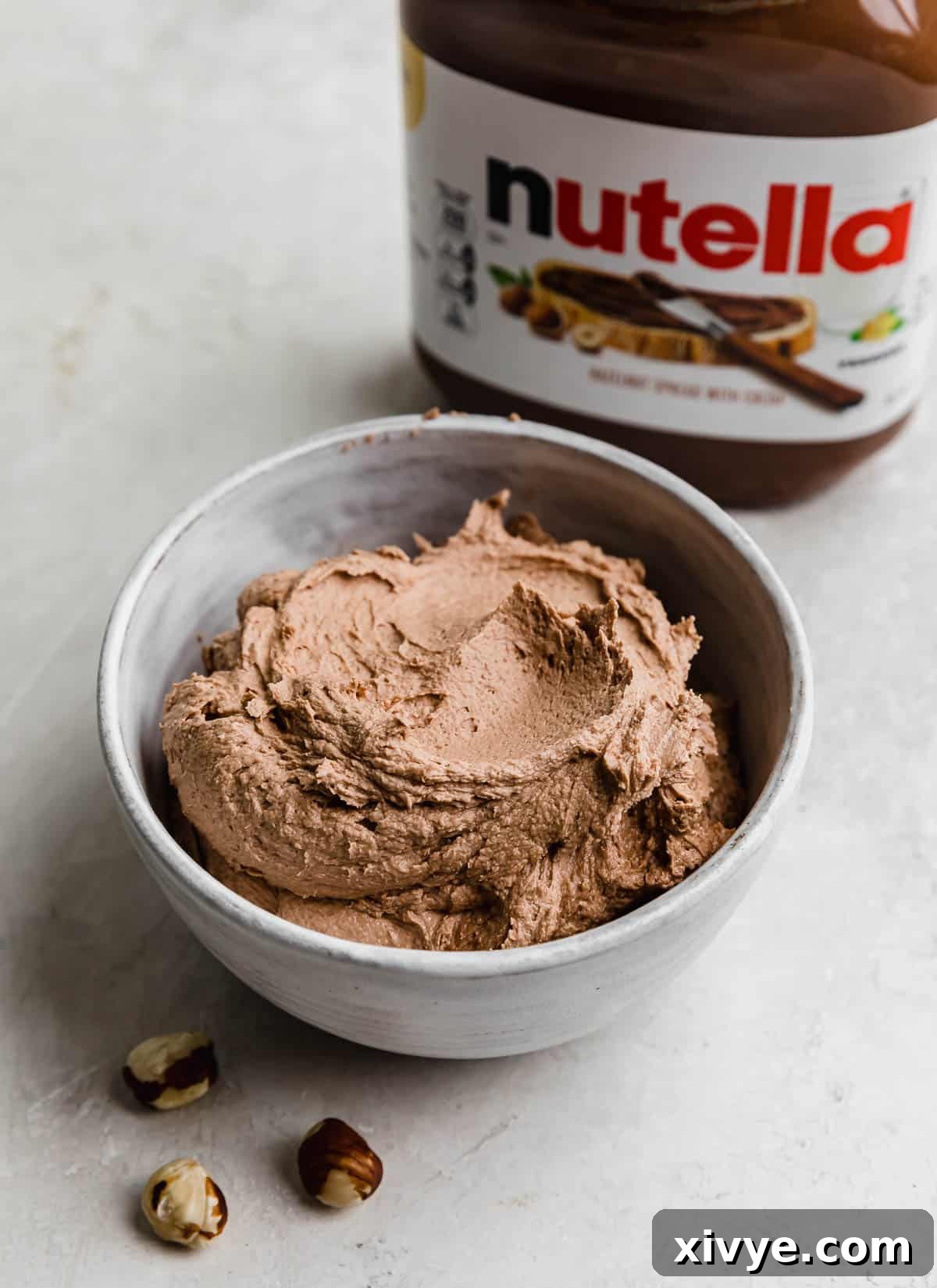 Decadent Nutella Frosting 2 A white bowl filled with the best Nutella Frosting and a bottle of Nutella in the background.