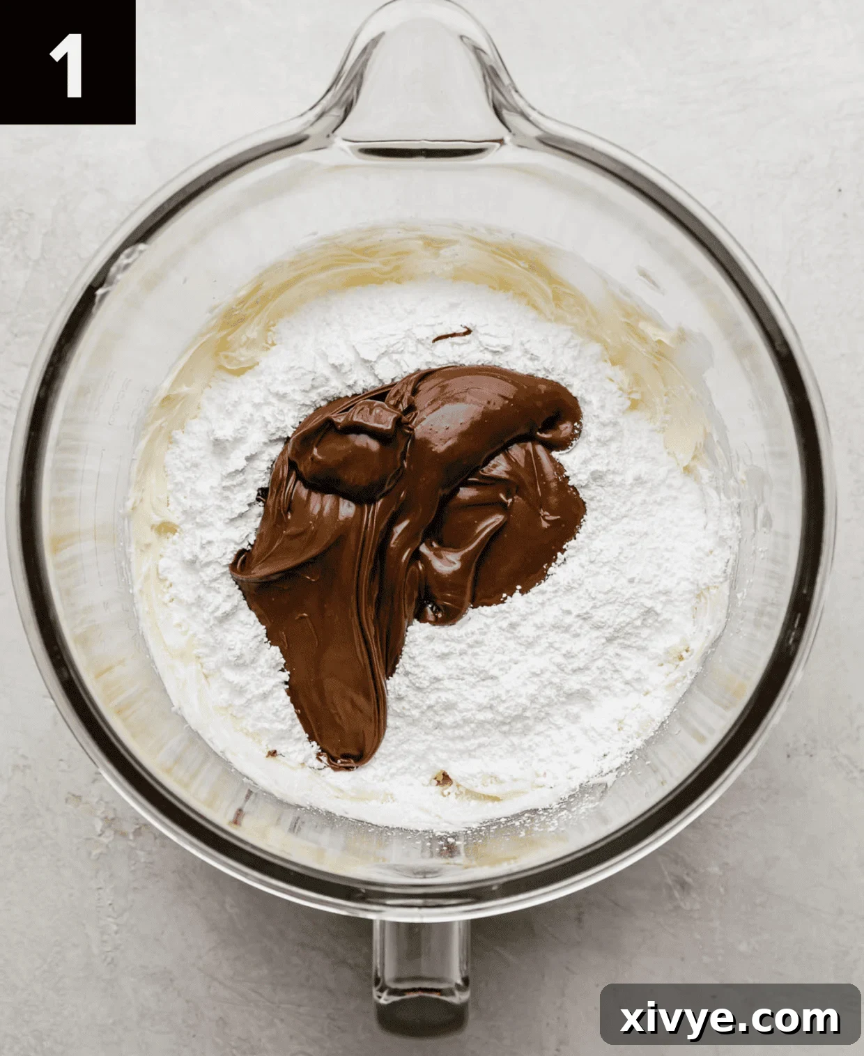Decadent Nutella Frosting 4 A glass mixing bowl with butter, powdered sugar, and Nutella in it (on a white background).