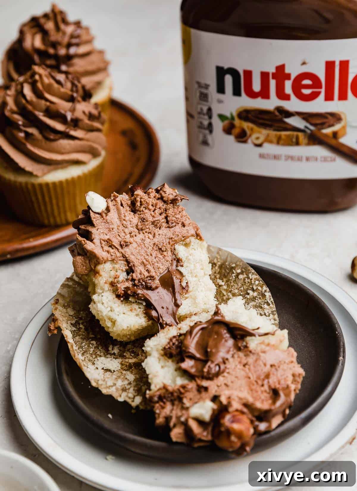Decadent Nutella Swirl Cupcakes 6 A Nutella Cupcake on a black plate cut in half, showing the inside filled with Nutella.