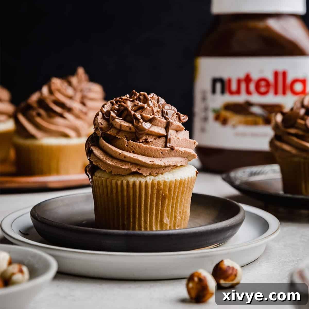 Decadent Nutella Swirl Cupcakes 7 A Nutella Cupcake on a black plate with a Nutella jar in the background.