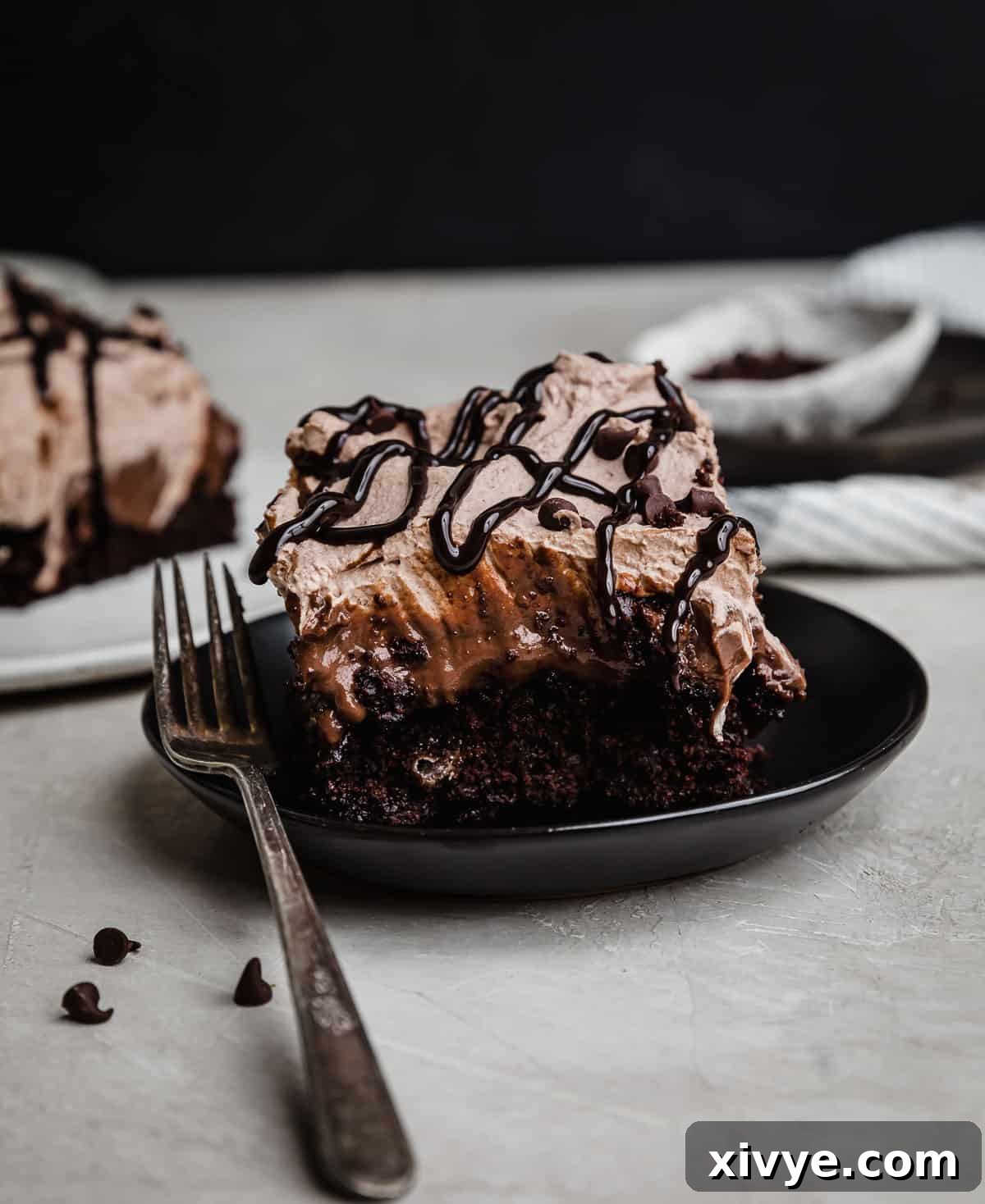 Chocolate pudding cake (Chocolate Poke Cake recipe) on a black plate, topped with whipped cream and chocolate sauce.