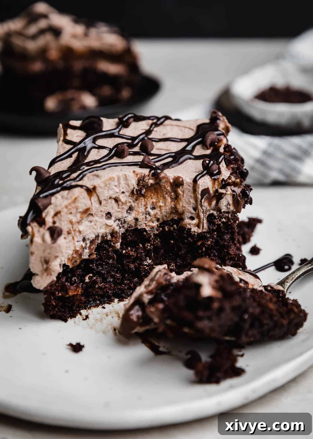 A bite taken out of a Chocolate Poke Cake that's on a white plate.
