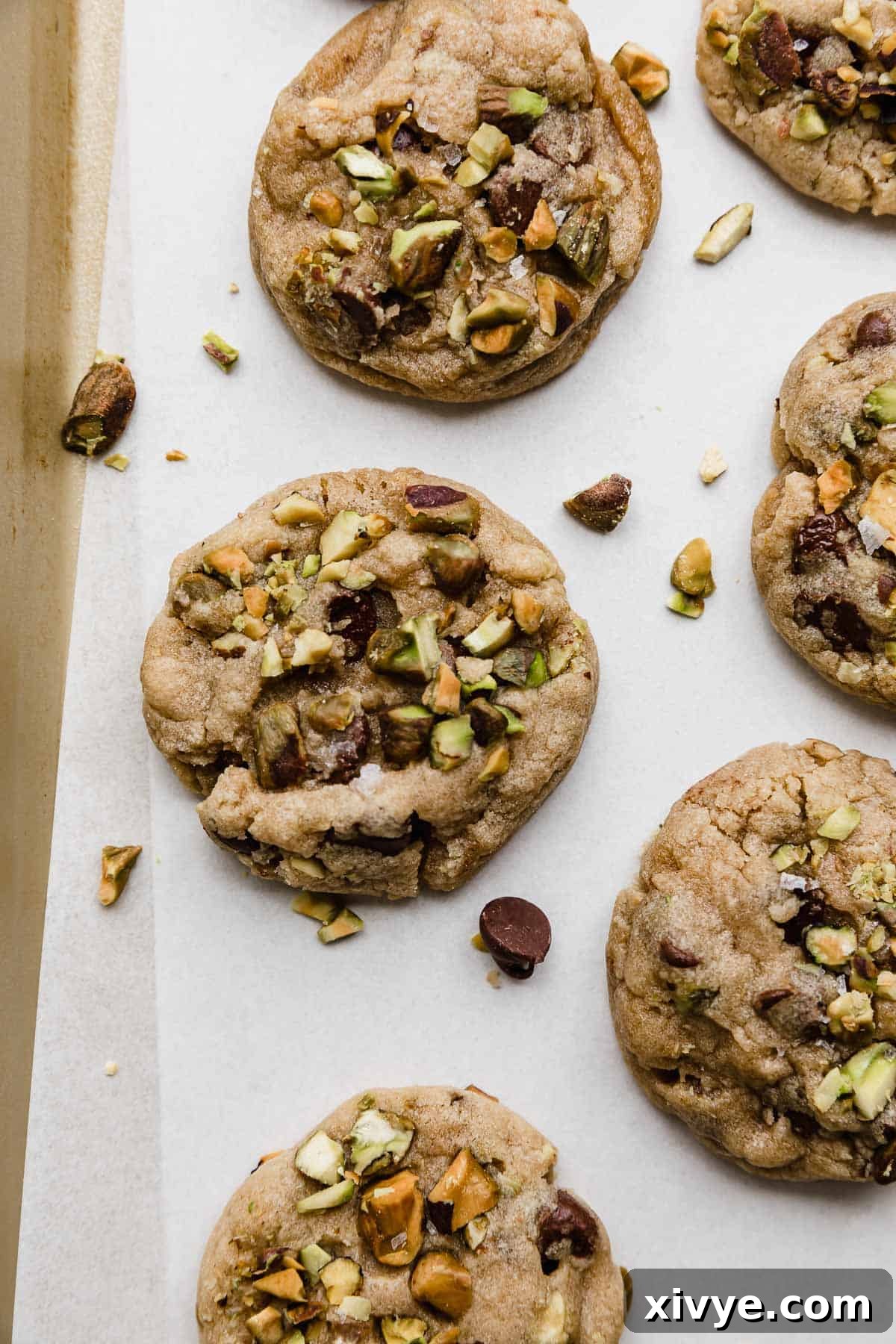 Emerald Pistachio Chocolate Chip Cookies 2 Chocolate Chip and Pistachio Cookies on a white parchment paper.