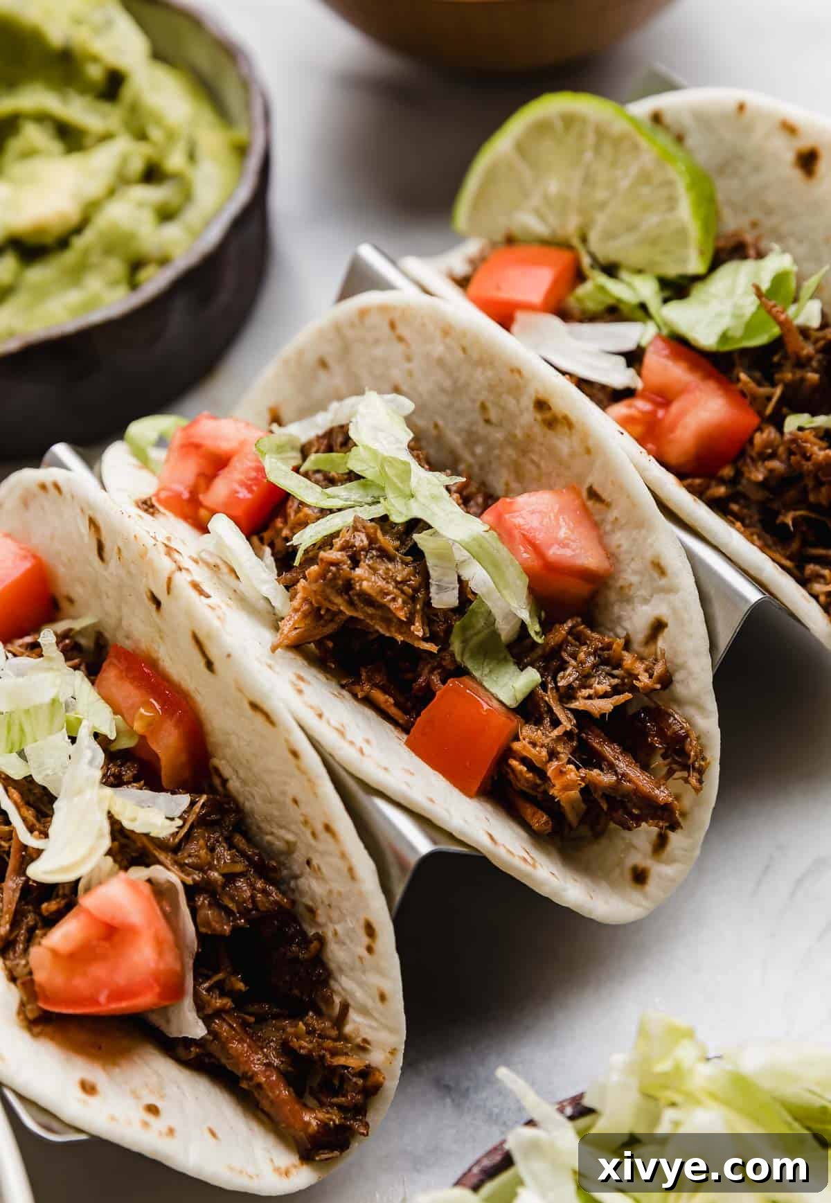 Three shredded beef tacos (made in the crock pot) topped with lettuce, tomato and guacamole.