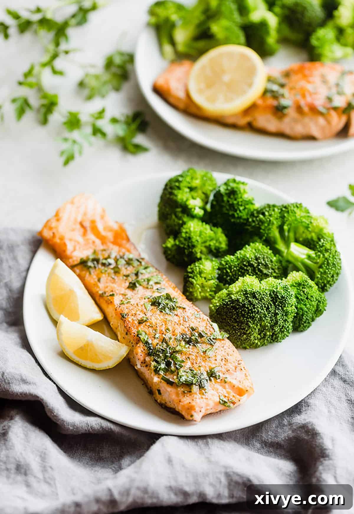 Lemon Honey Glazed Salmon is the perfect pan seared salmon recipe. The sweet lemon honey glaze is packed with fresh parsley, chives, and lemon. This is a healthy dinner recipe AND an easy recipe at that! #saltandbaker #salmon #healthyrecipes A seared Lemon Honey Glazed Salmon fillet on a white plate, garnished with fresh herbs and a lemon wedge.