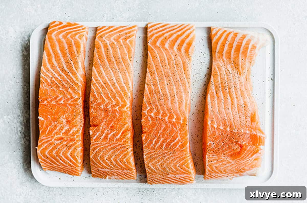 Lemon Honey Glazed Salmon is the perfect pan seared salmon recipe. The sweet lemon honey glaze is packed with fresh parsley, chives, and lemon. This is a healthy dinner recipe AND an easy recipe at that! #saltandbaker #salmon #healthyrecipes Four raw salmon fillets, patted dry and seasoned with salt and pepper, arranged on a white cutting board.