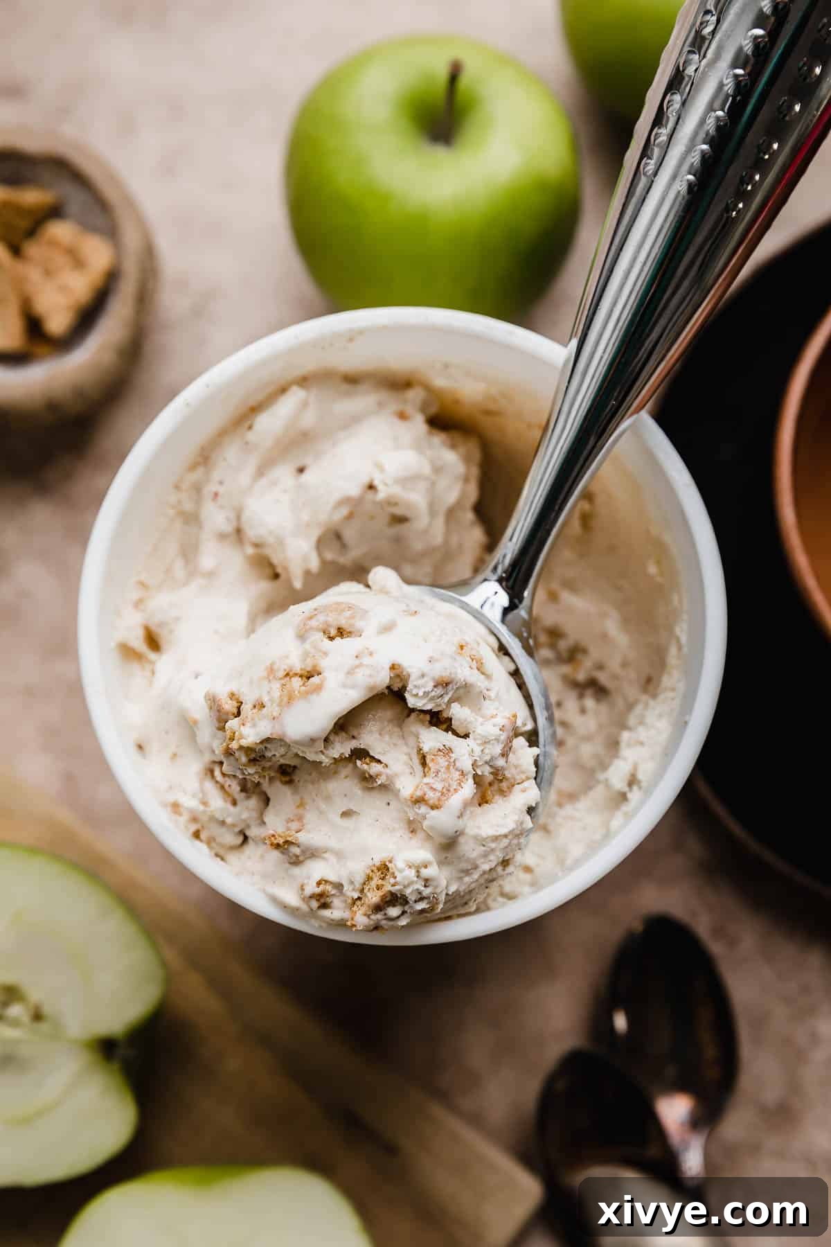 An ice cream scoop filled with homemade Apple Pie Ice Cream with Granny Smith apples in the background.