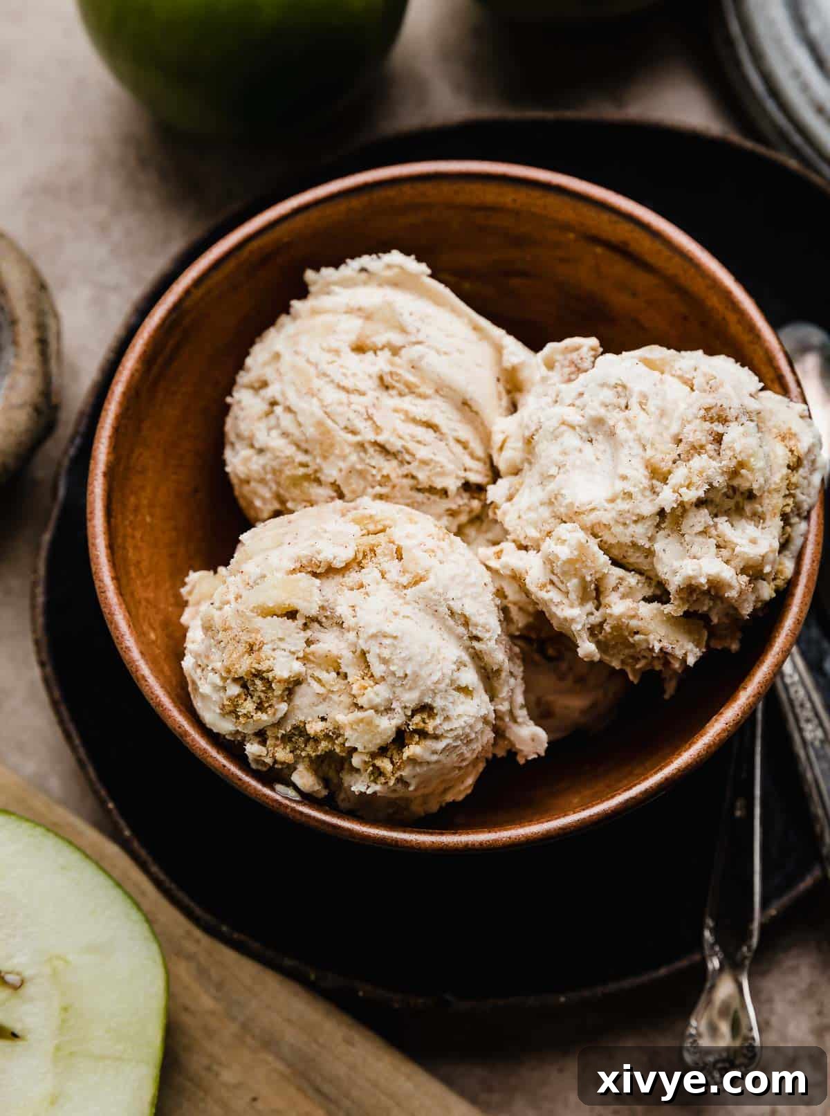 Three scoops of Apple Pie Ice Cream studded with cinnamon apples and cinnamon graham cracker pieces in a brown bowl.